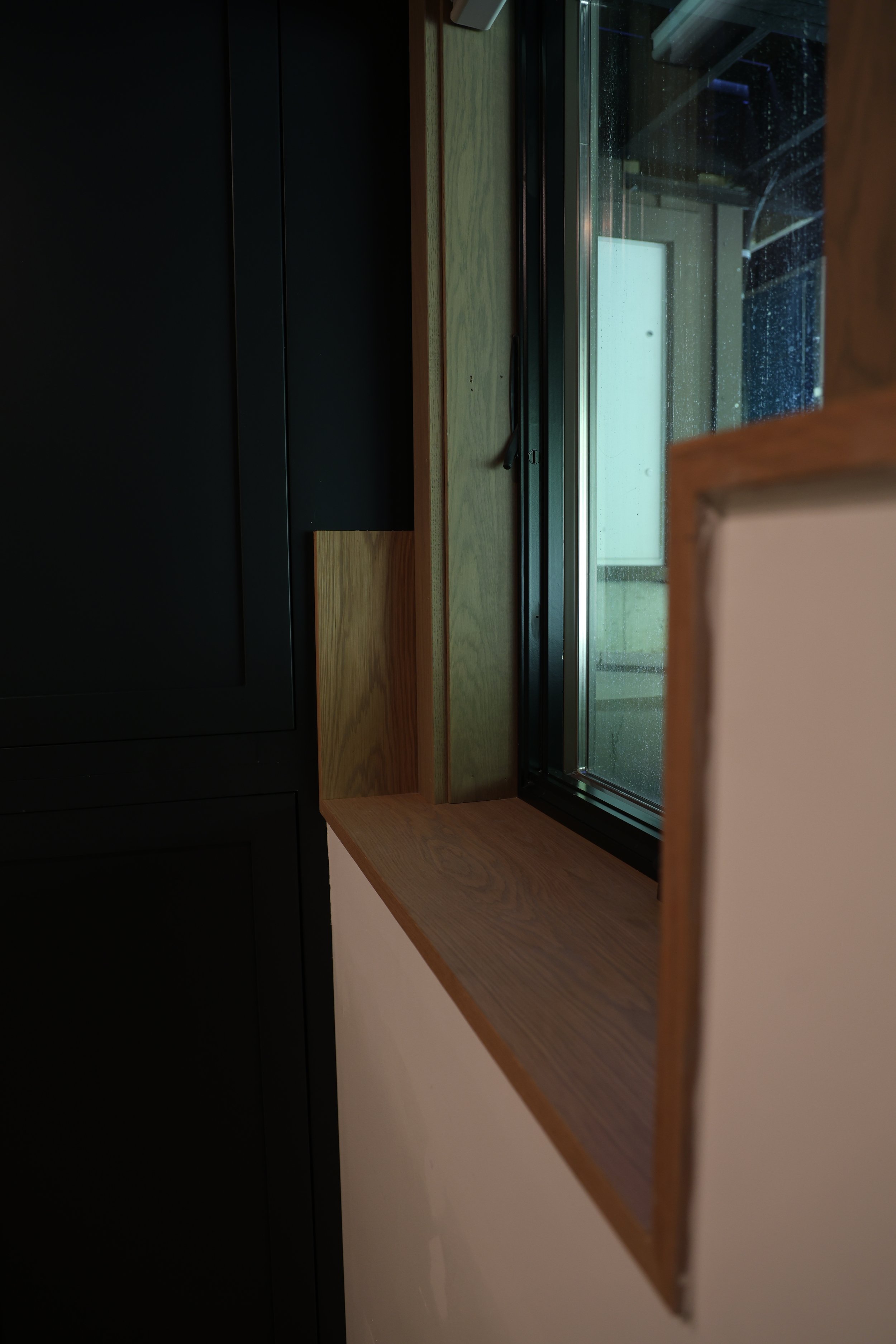 A wooden windowsill with a black cabinet beside it and a window with raindrops on the glass, showing a blurred outdoor scene.