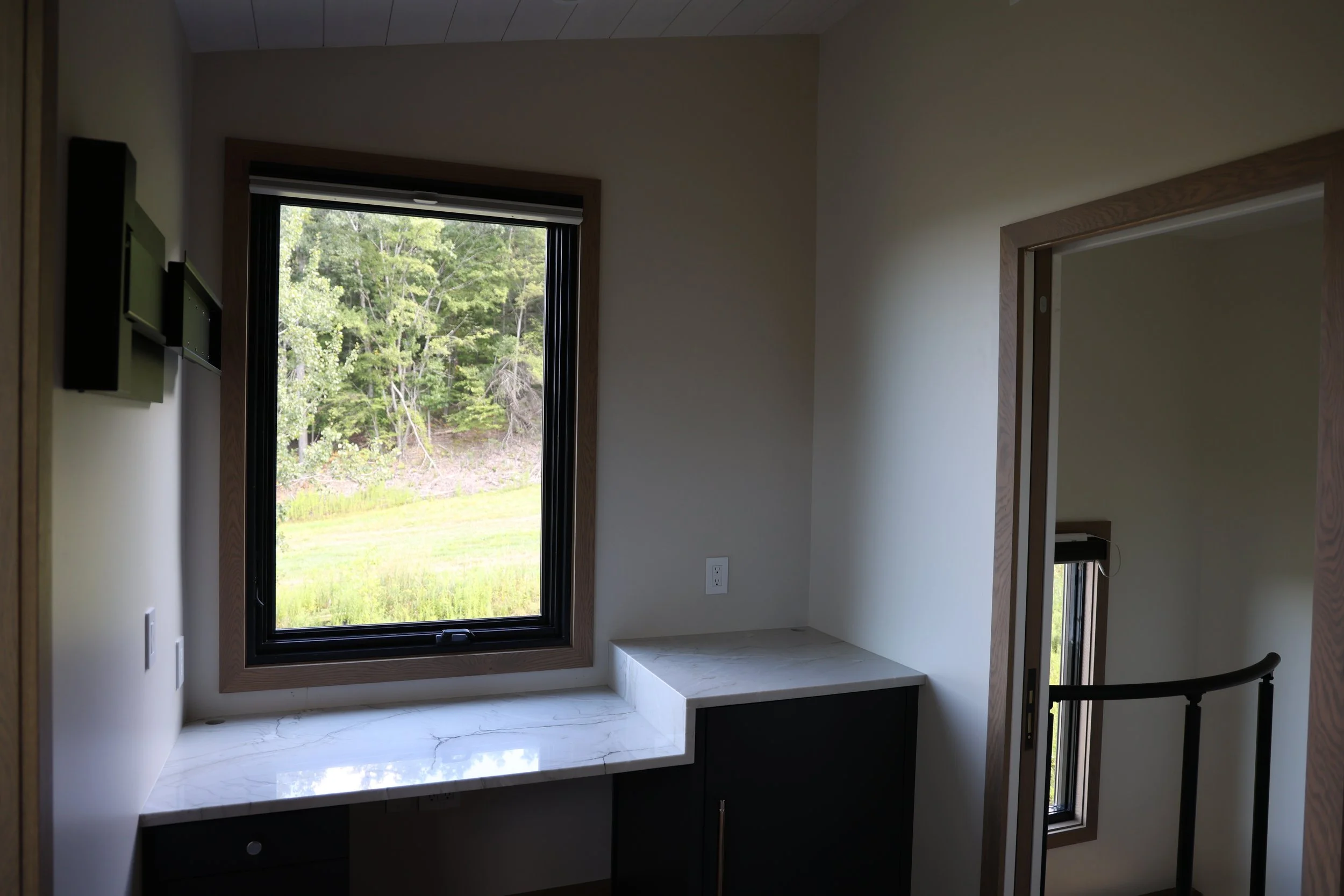 Room with large window overlooking green trees, built-in marble desk, and cabinetry underneath in Ellicottville, NY. Part of a staircase with Viewrail staircase visible.