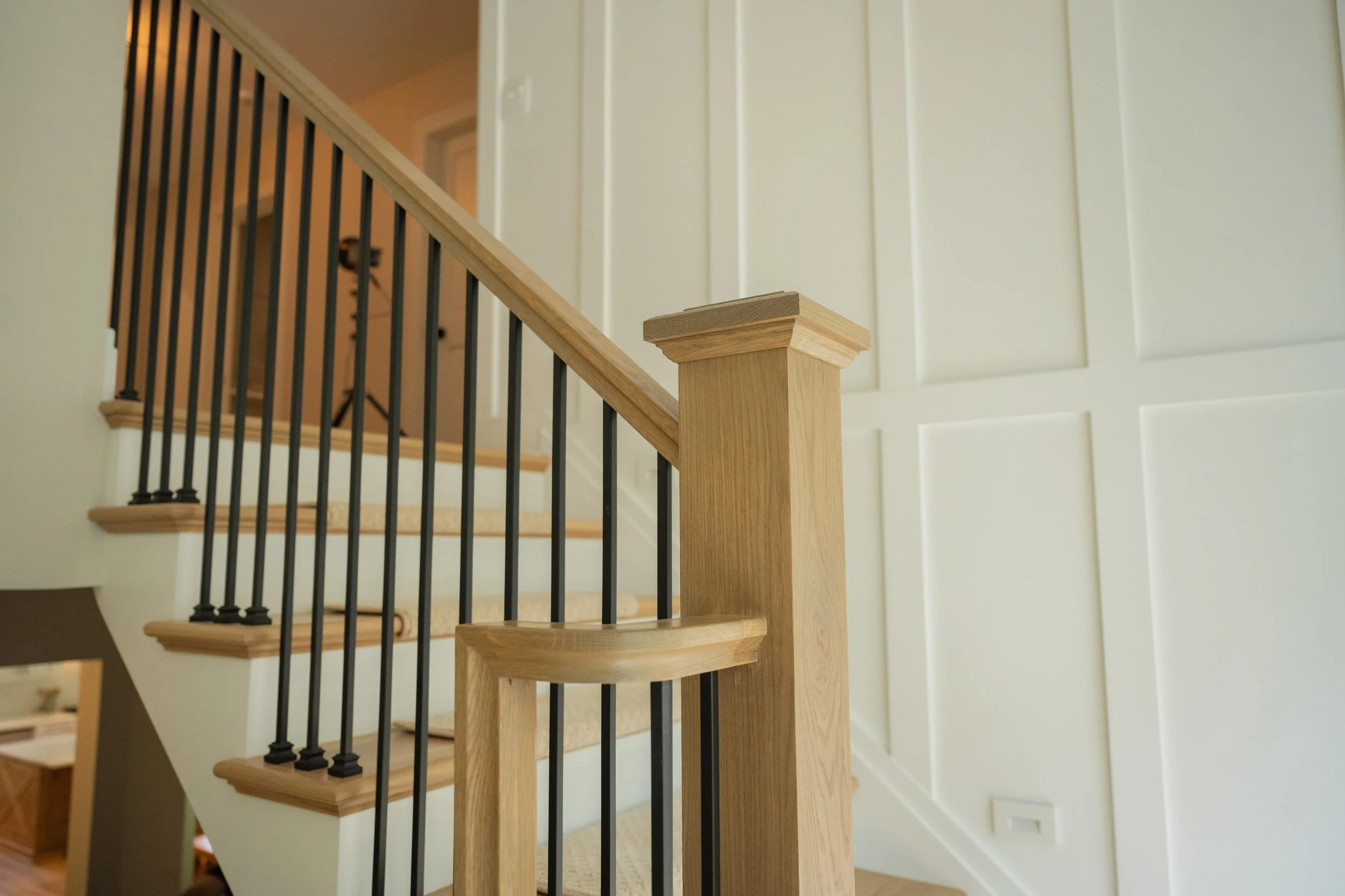 Interior view of a staircase with wooden handrail and black metal balusters in a modern home, with beige walls and a decorative wall panel.