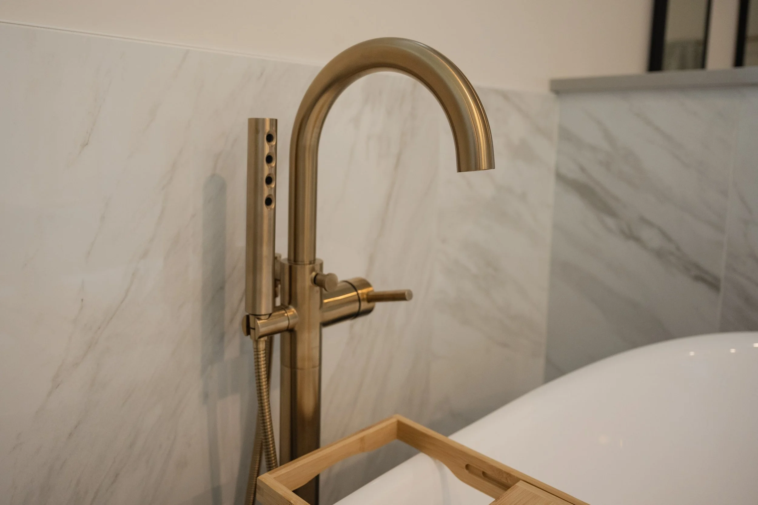Brushed gold kitchen faucet with a curved spout and a single lever handle, mounted on a white marble countertop with a matching marble backsplash.