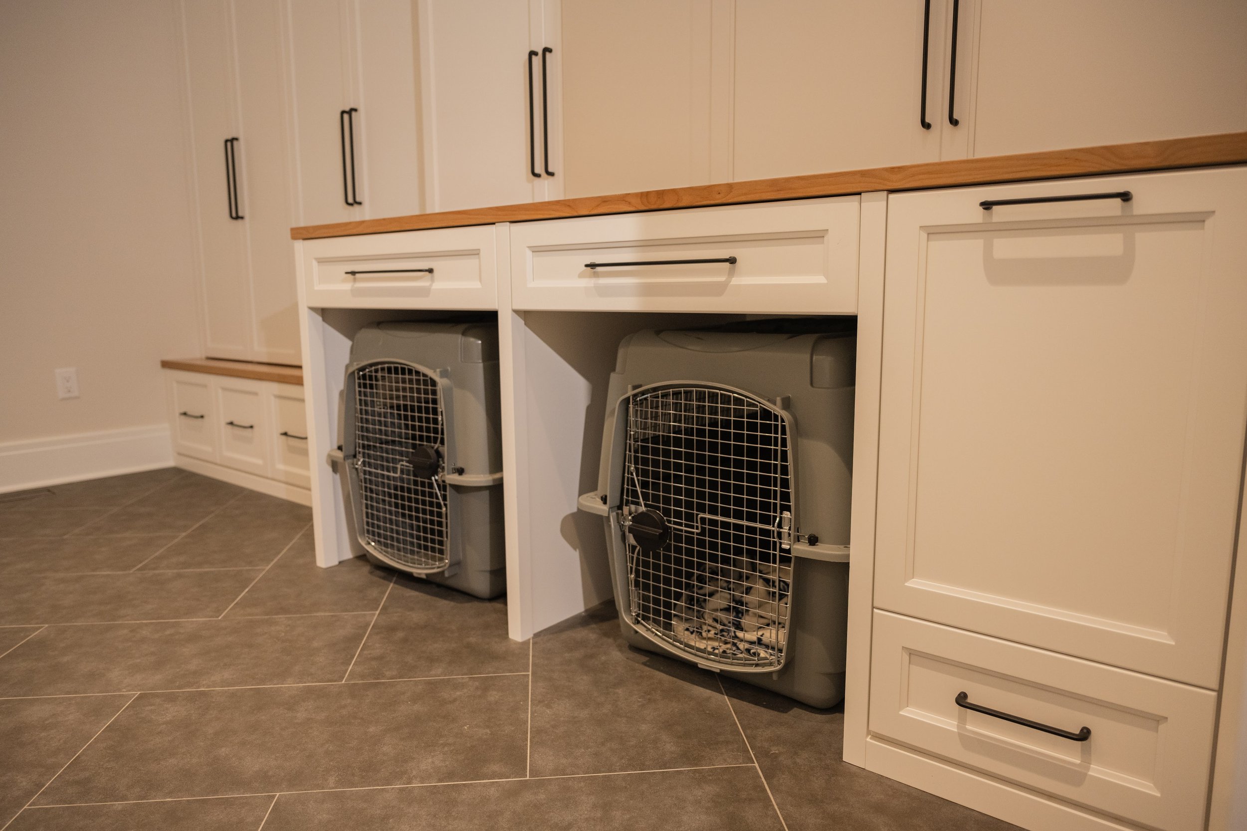 Kitchen with white cabinets, black handles, wooden countertop, and two pet crates on the floor.