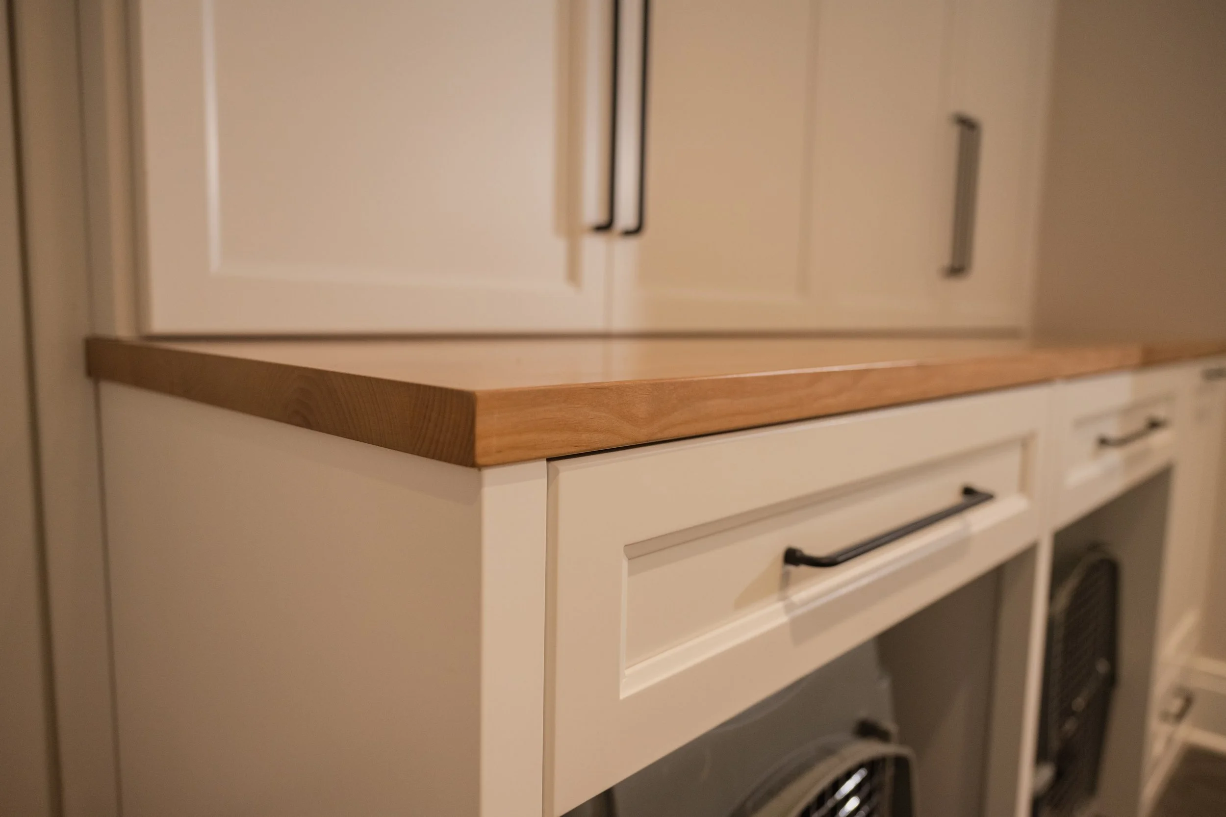 Close-up of white kitchen cabinets with black handles and a wooden countertop.
