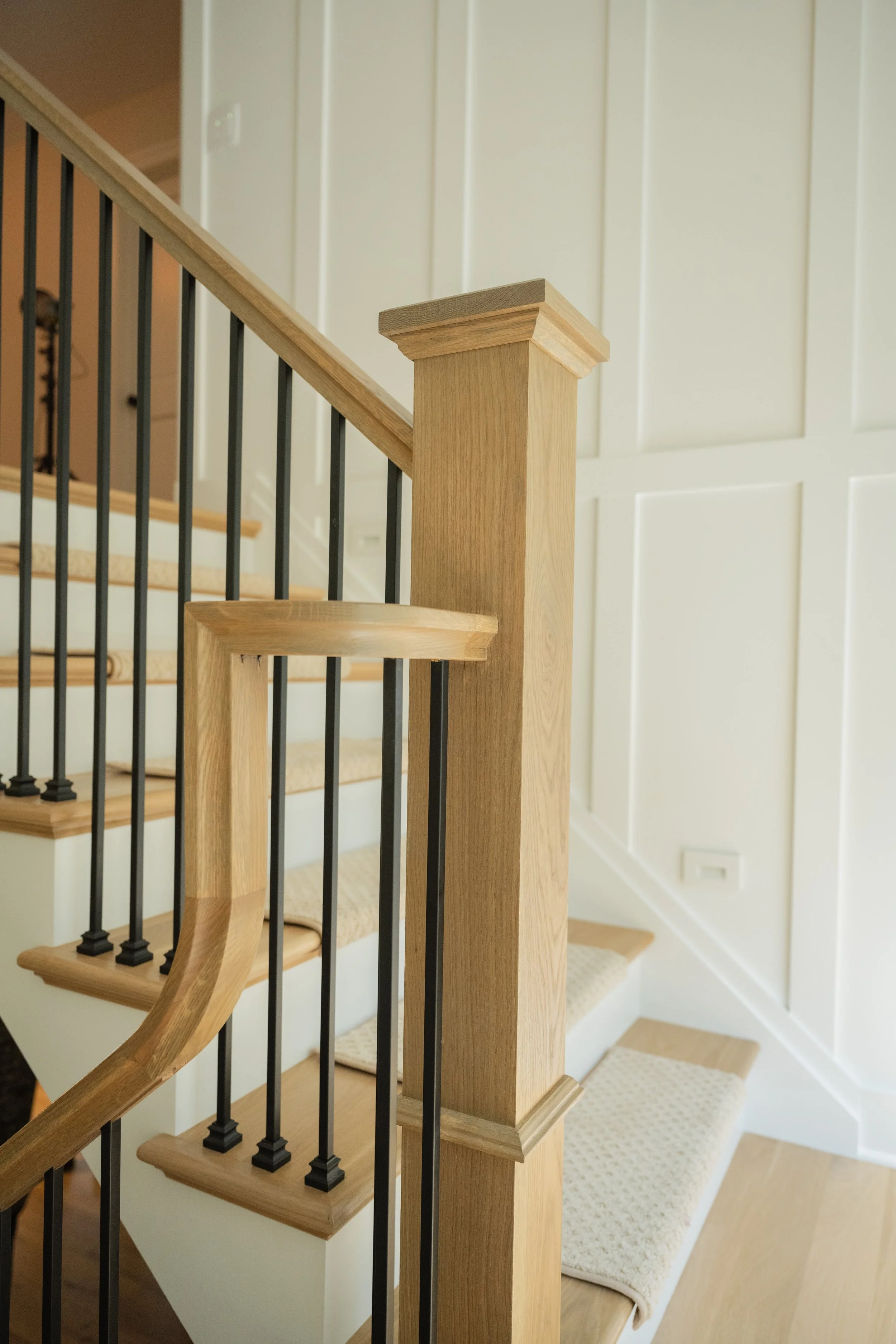 Wooden staircase handrail with black balusters and beige carpeted steps in a home interior.