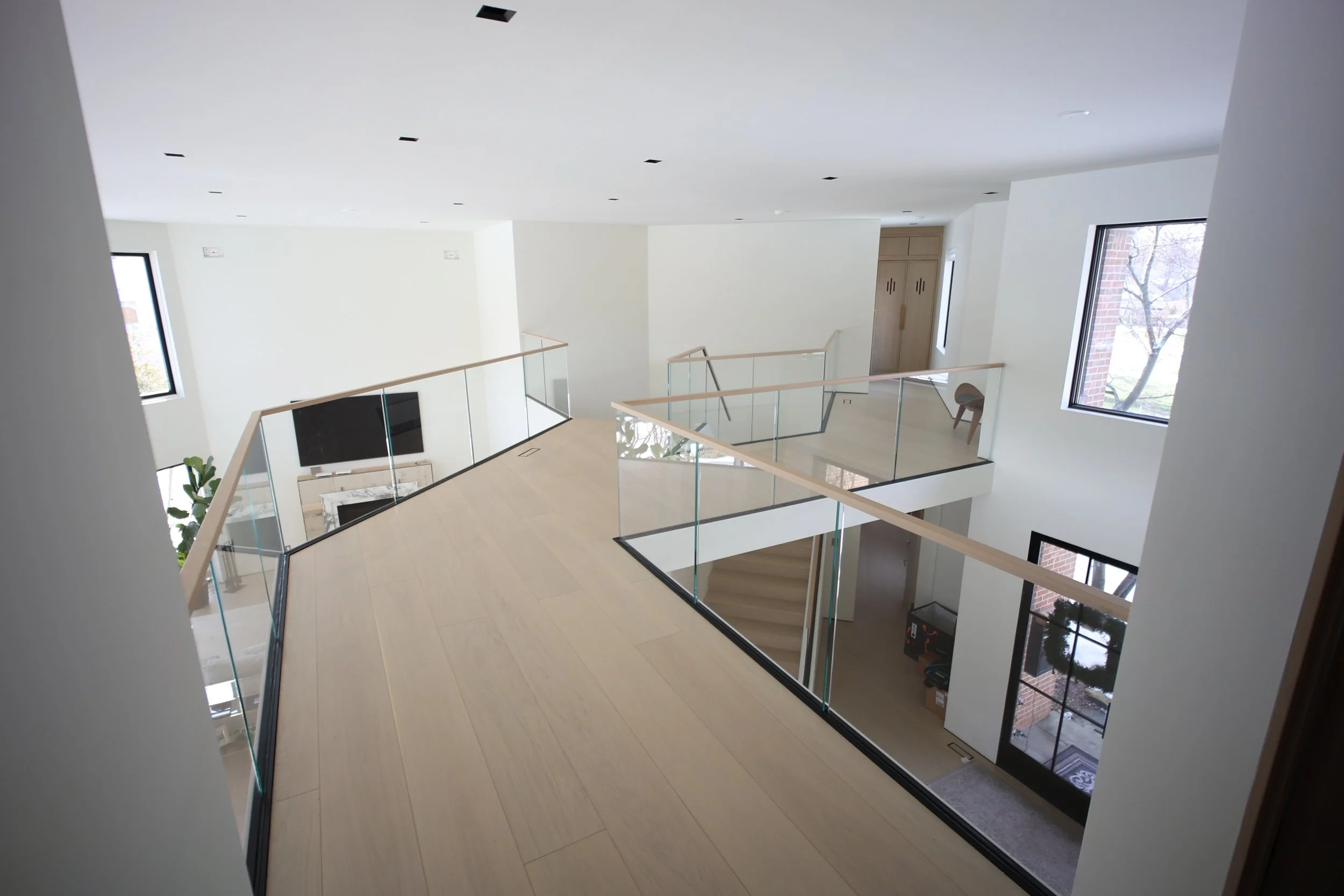 A modern, open-concept interior of a multi-story home with a view of the second floor and staircase, large windows, light-colored flooring, and minimal decor.