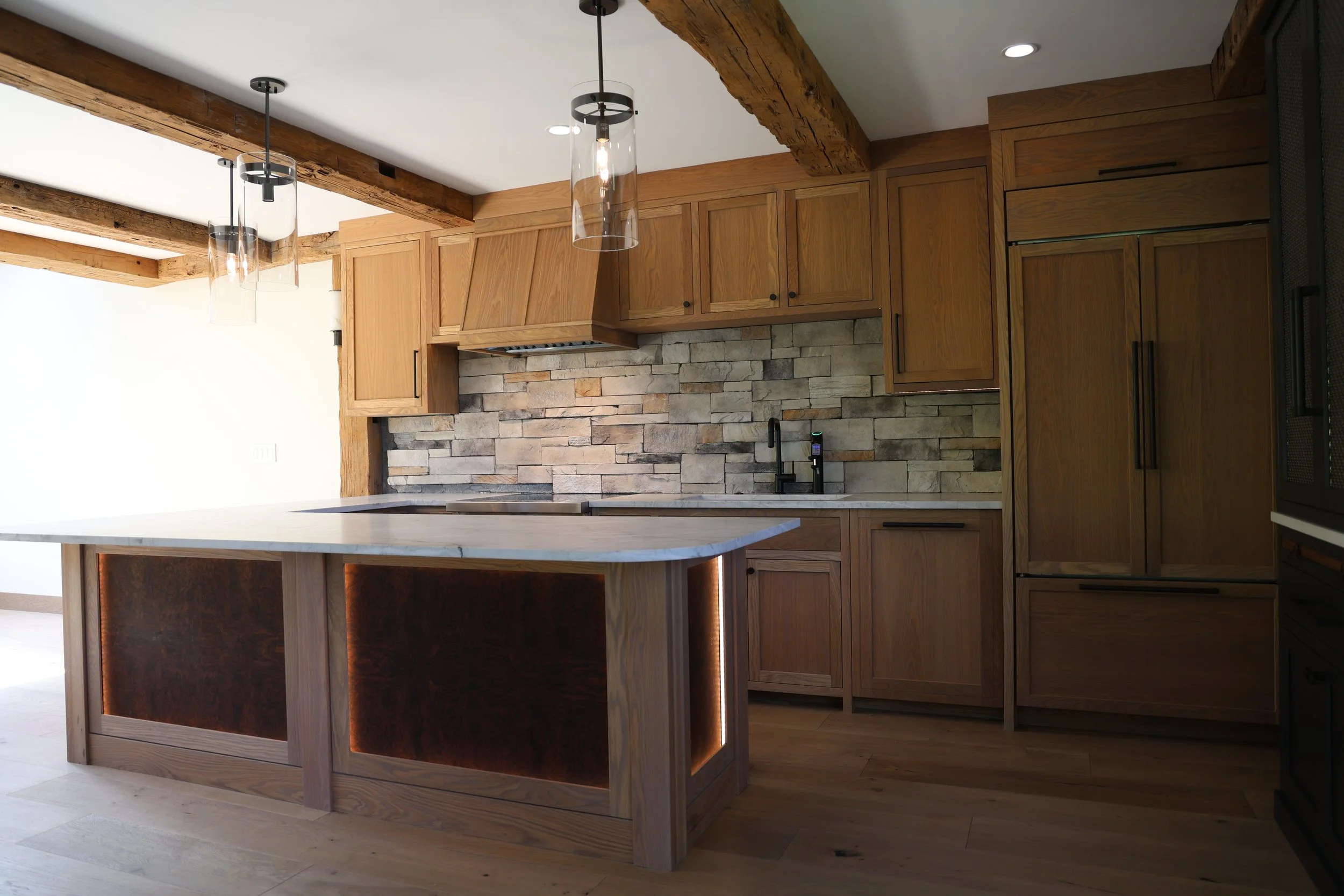 Modern kitchen with wooden cabinets, stone backsplash, island with a marble top, and pendant lights.