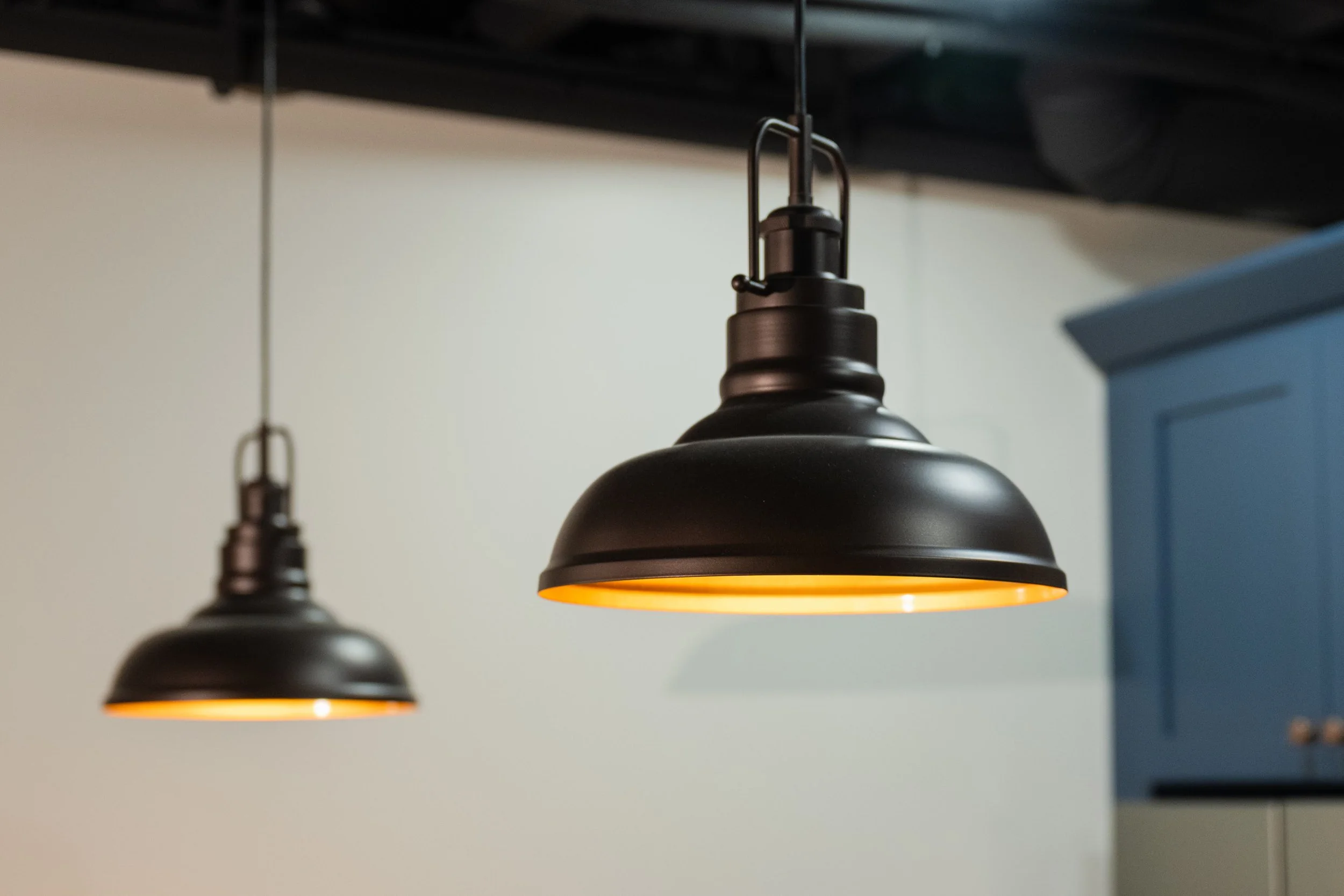 Black pendant lights hanging from the ceiling with warm yellow interior lighting, against a neutral wall background.
