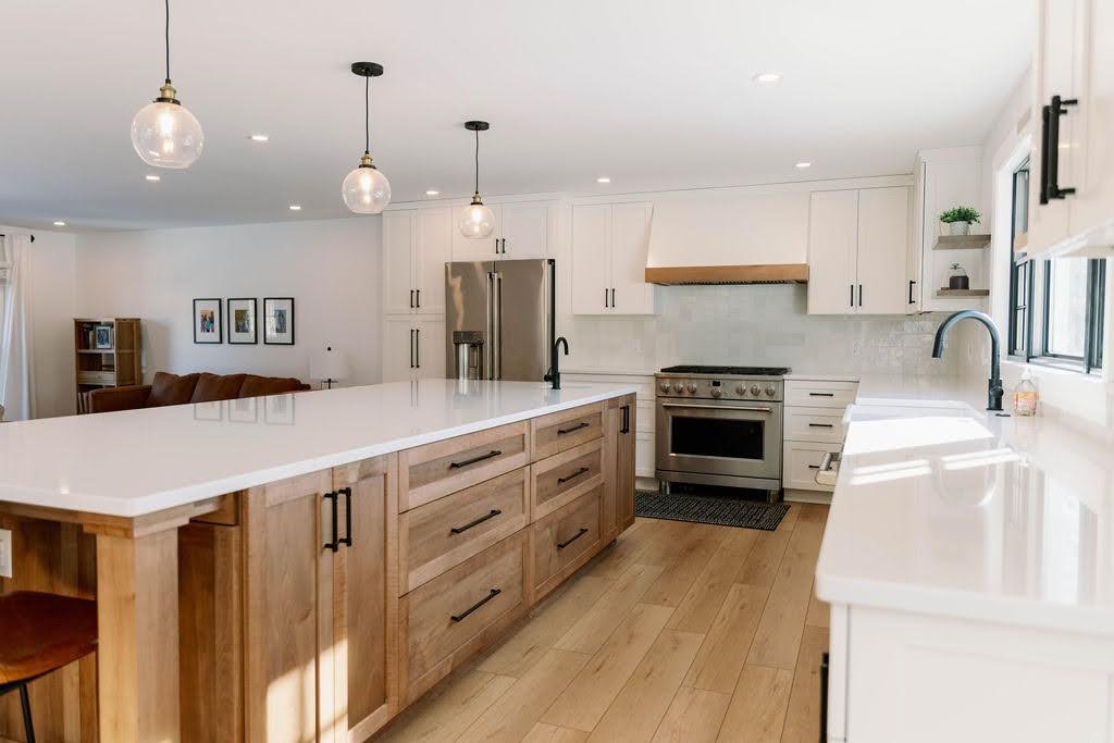 Modern kitchen in Buffalo, NY with white cabinets, white quartz countertop island, stainless steel appliances, pendant lights, and hardwood flooring.