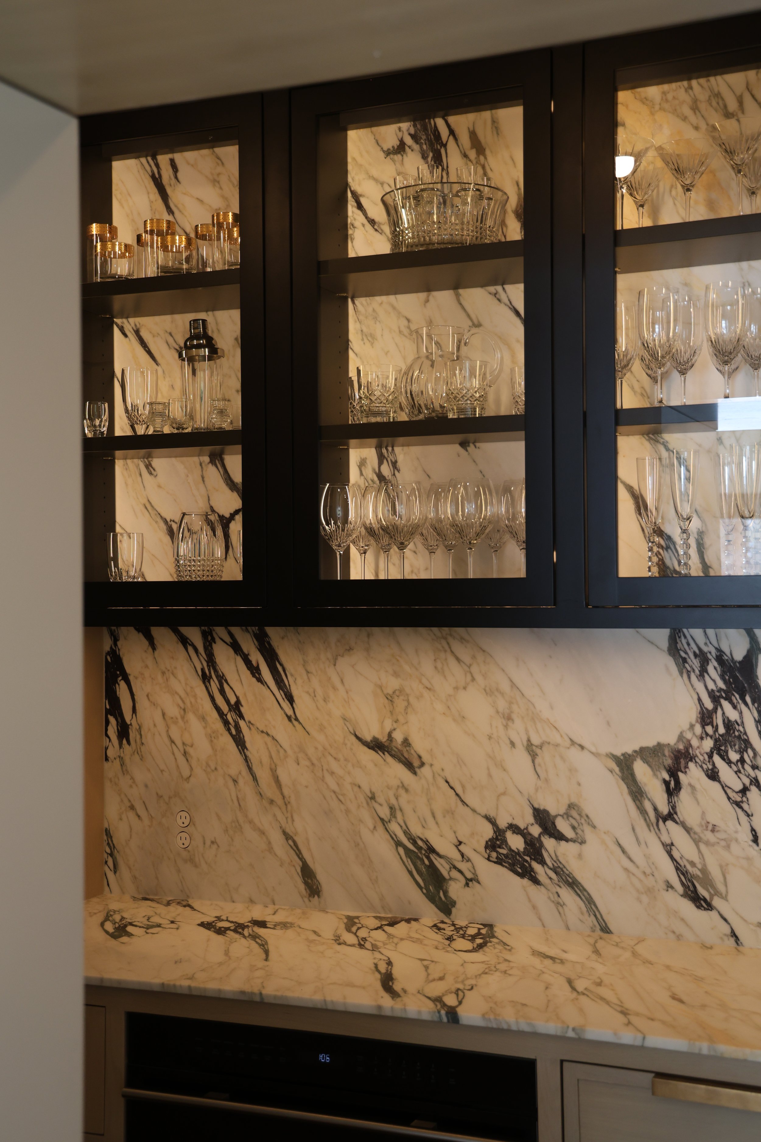 Kitchen with black cabinets and a black and white marble backsplash and countertop. The countertop displays various glassware, including wine glasses, champagne flutes, and decorative glass bowls.