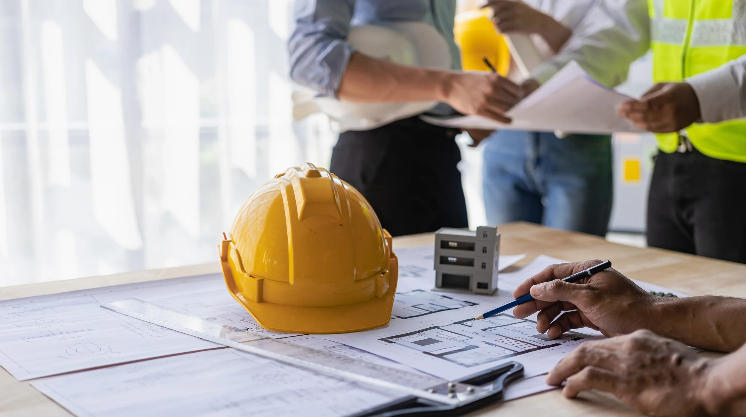 Ein gelber Schutzhelm und Baupläne auf einem Schreibtisch, die symbolisch für Sicherheit, sorgfältige Planung und den verlässlichen Schutz Ihrer Daten stehen.