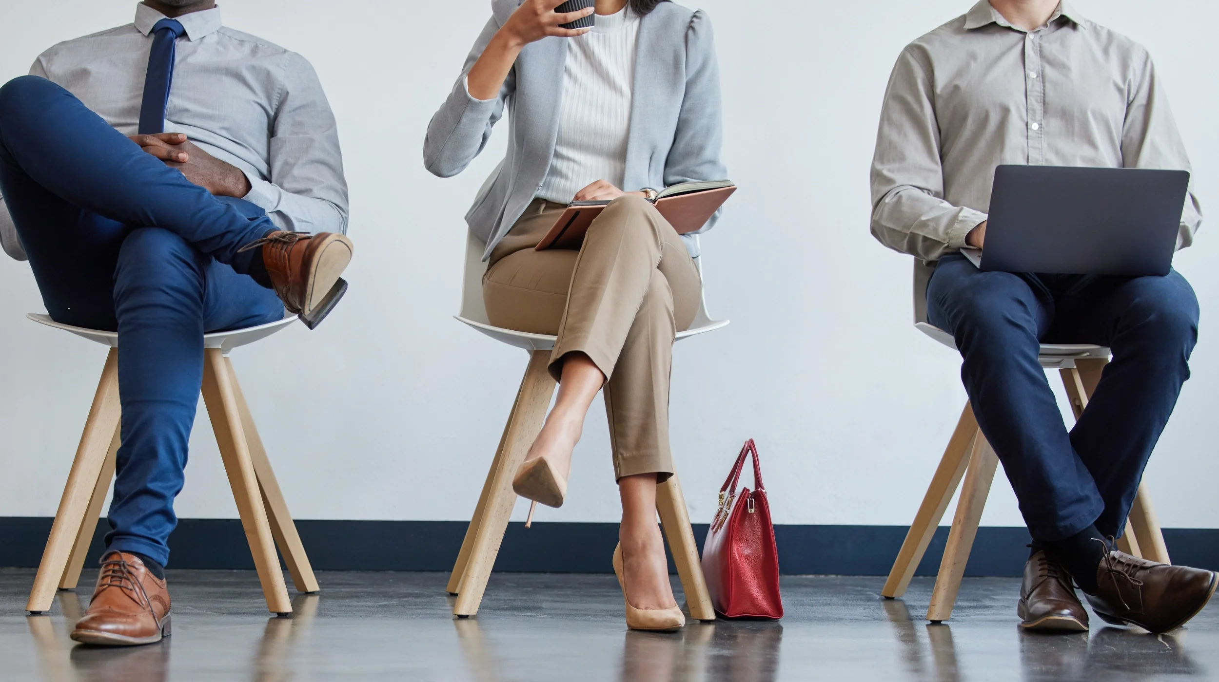 Drei professionell gekleidete Personen sitzen nebeneinander auf Stühlen, stellvertretend für neue Talente und Bewerber, die ihre Karriere in unserer Einkaufsberatung starten.