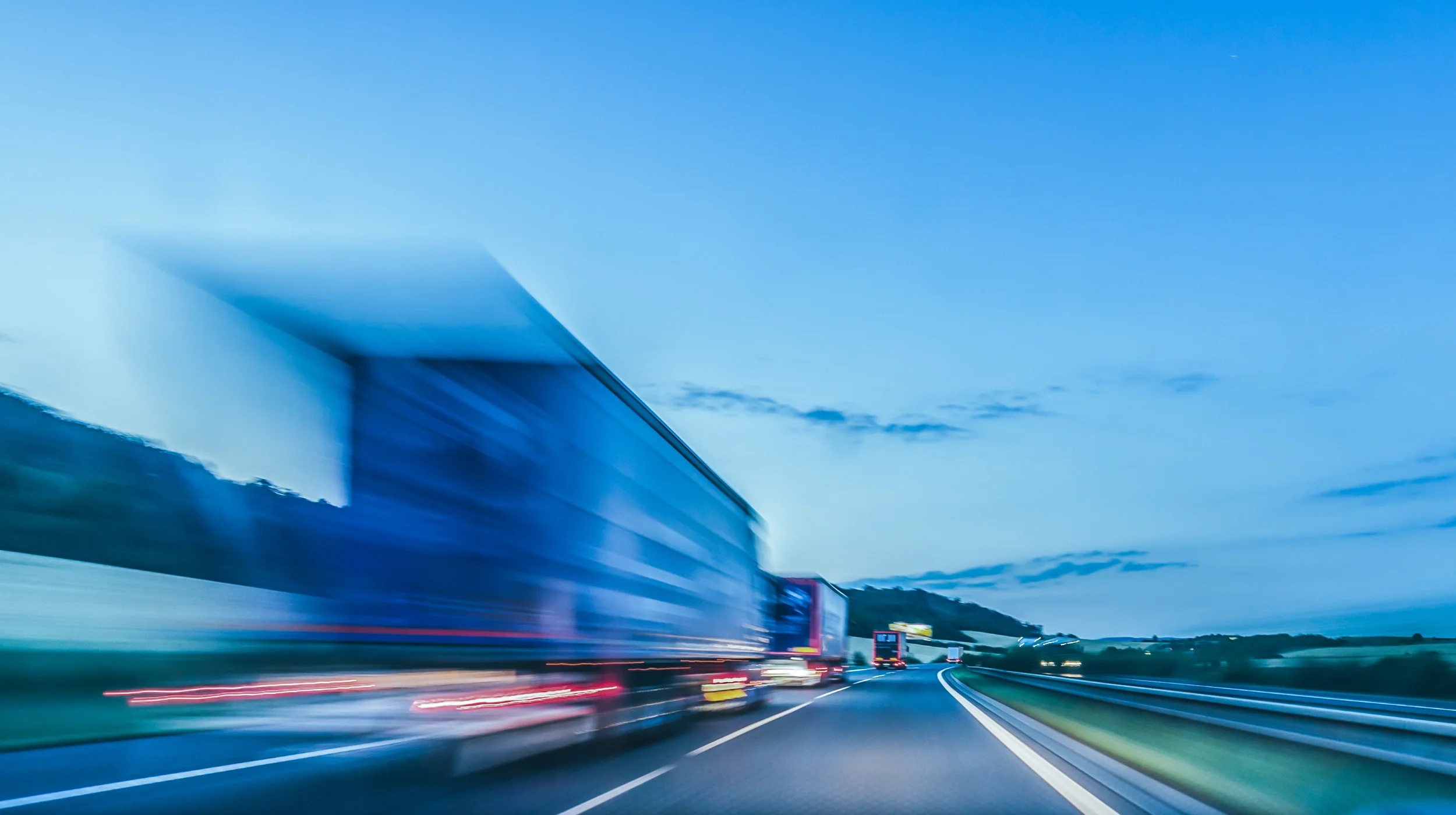Ein schnell fahrender LKW auf einer Autobahn in der Dämmerung, der für optimierte Frachtkosten, reibungslose Logistik und dauerhafte Wertschöpfung im Unternehmen symbolisiert.