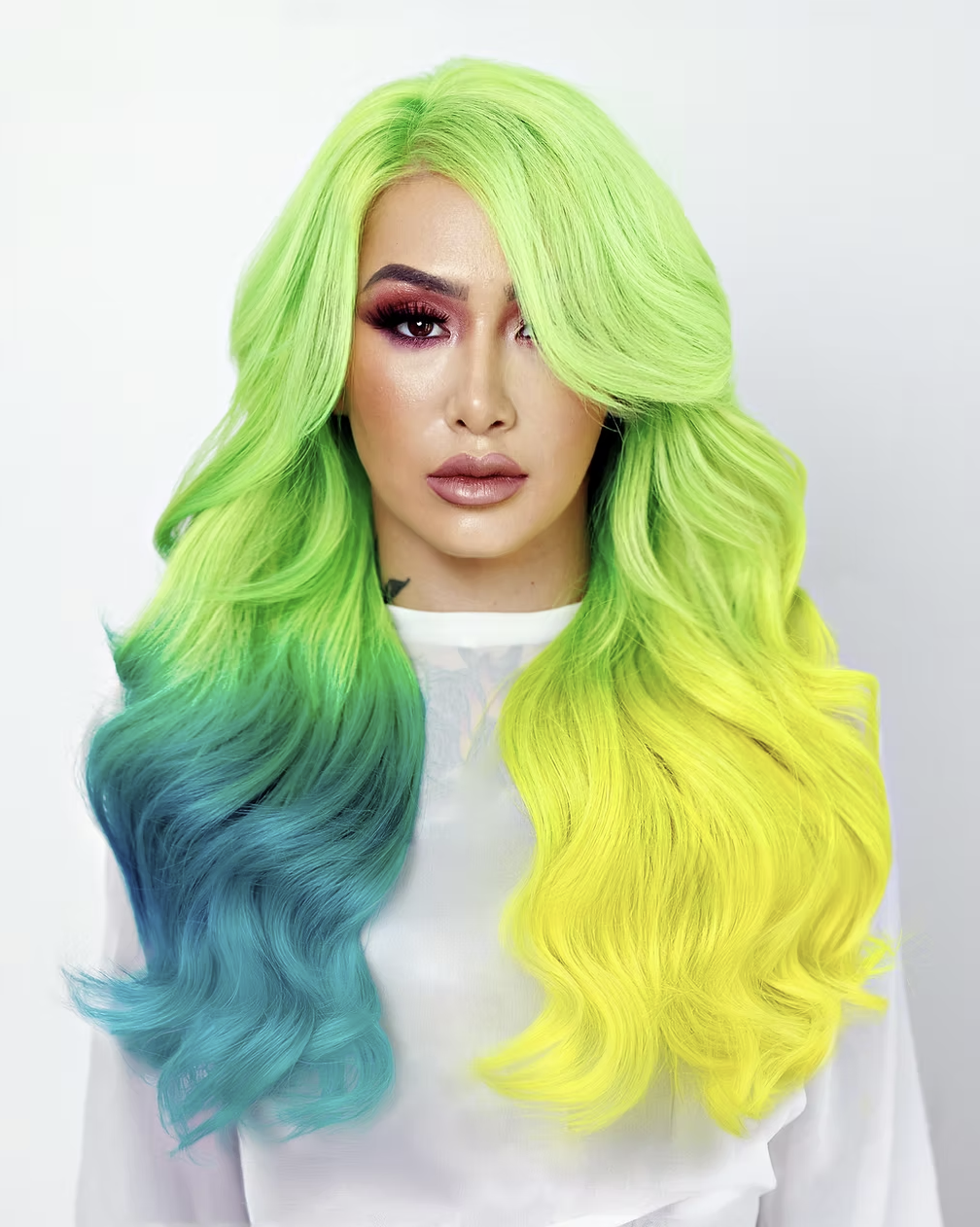 A woman with long, wavy neon green hair that fades into blue on one side and yellow on the other side. Shotzi Blackheart for Salon amoura hair extensions and fantasy hair color