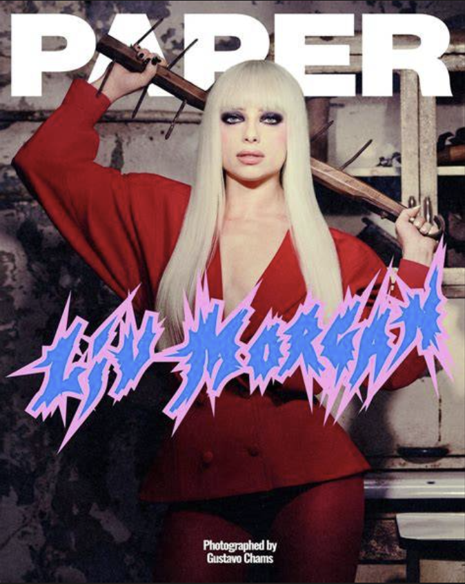 A woman with long platinum blonde hair and heavy makeup, wearing a red outfit, holding an axe over her shoulder. The background appears industrial or rustic, with text reading 'PAPER' and stylized, jagged text overlapping her chest saying 'LOVE FOREV