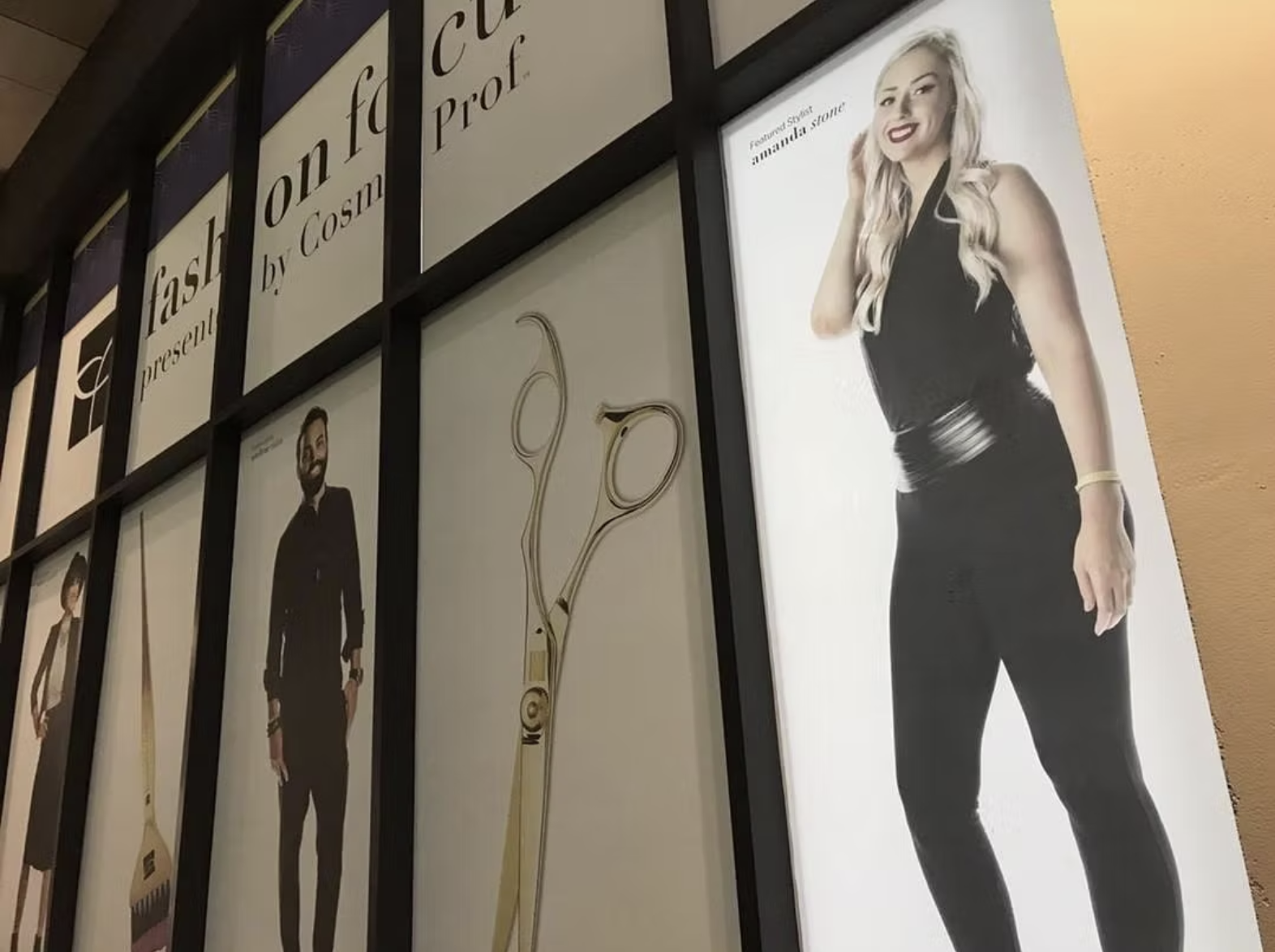 A wall display with framed posters, including a woman dressed in black with long wavy blonde hair, smiling and posing, and a man in a suit with glasses, standing with his hands in his pockets. The posters are part of a fashion or style presentation.