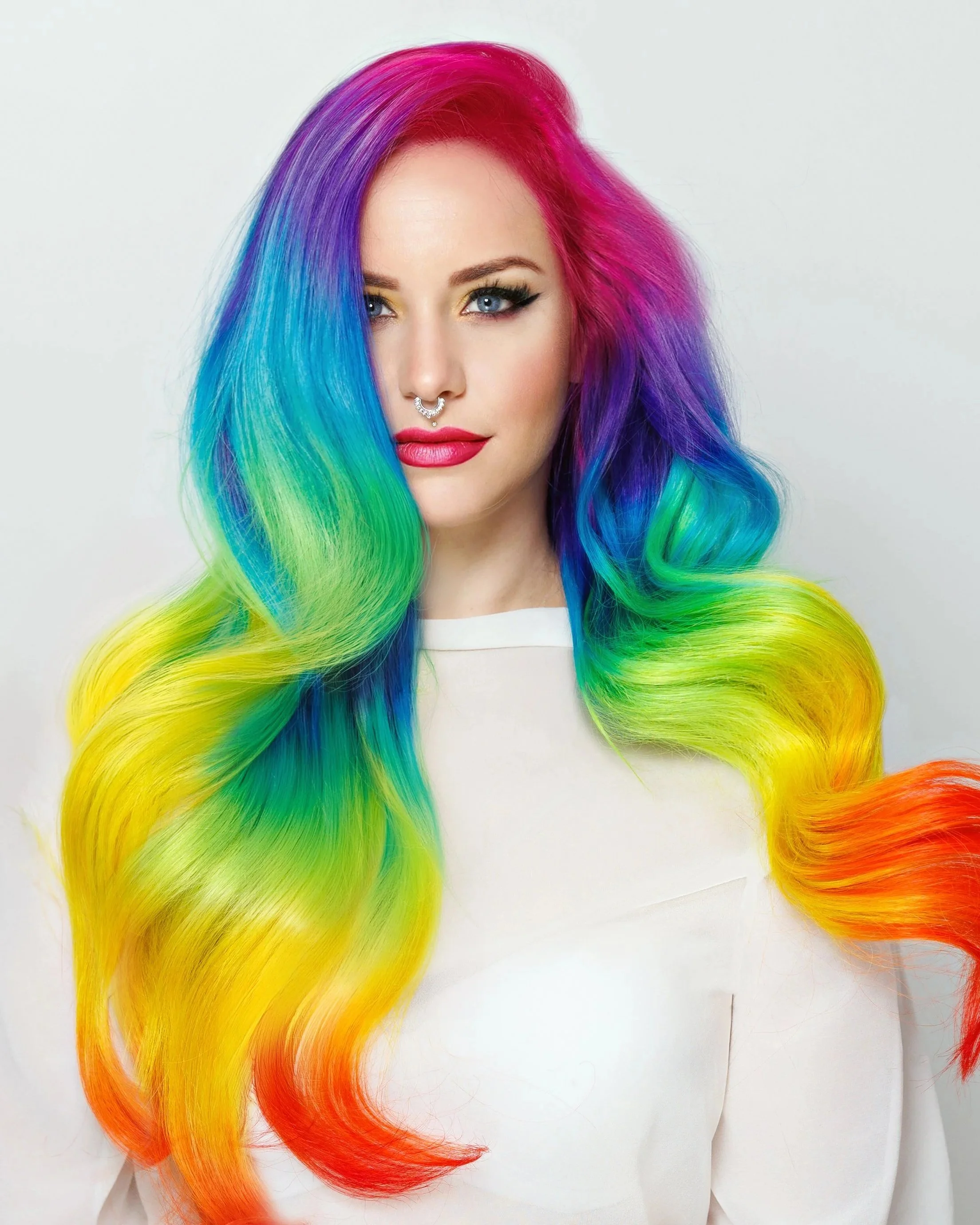 Woman with rainbow-colored hair, featuring shades of purple, blue, green, yellow, orange, and red, styled in long waves. Rainbow hair tinsel all done at Salon Amoura in Orlando Florida