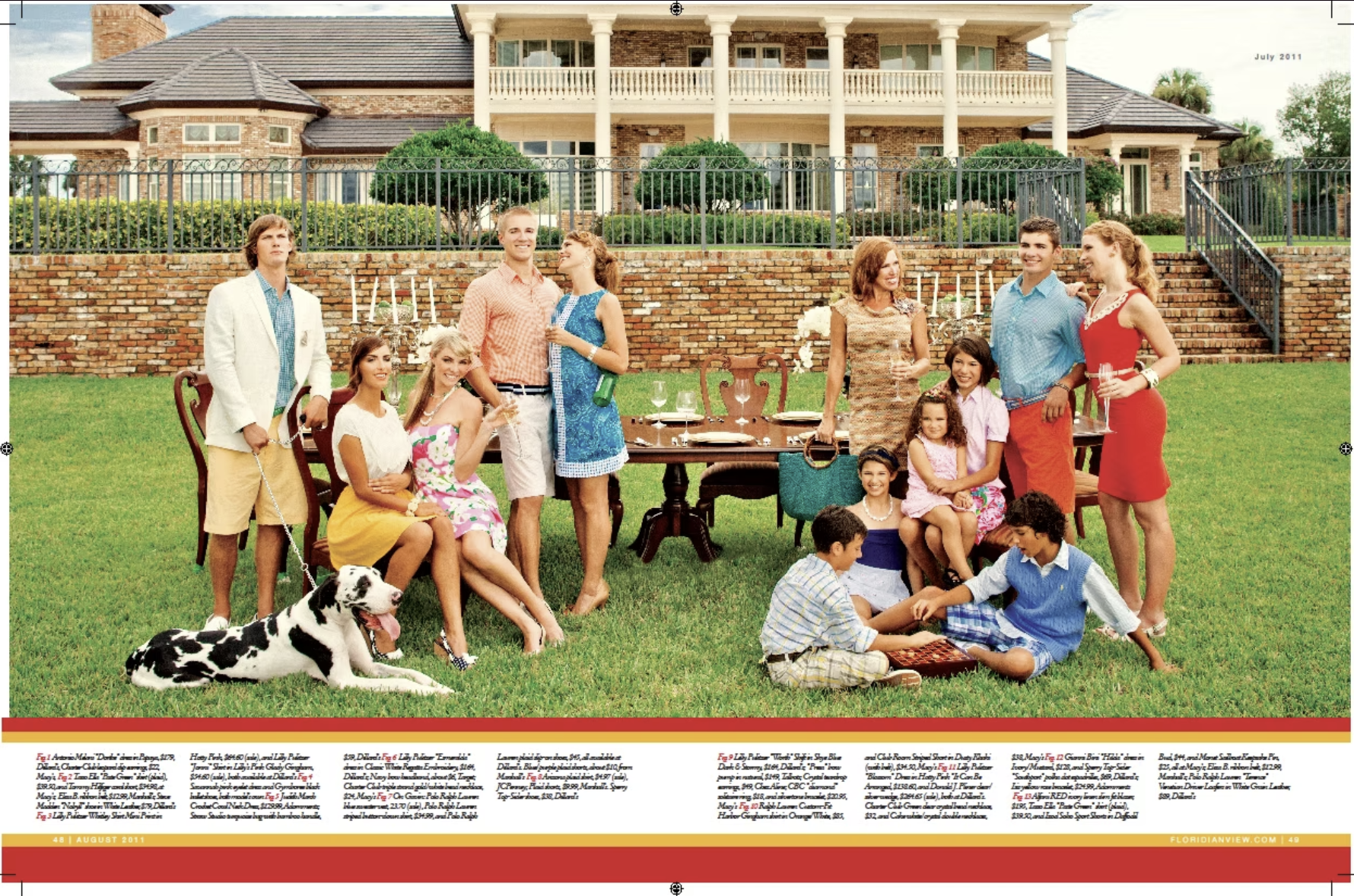 A group of people at a backyard gathering with a large house in the background. There are adults, children, a dog, and a decorated outdoor table with food and drinks. The scene appears festive and relaxed.