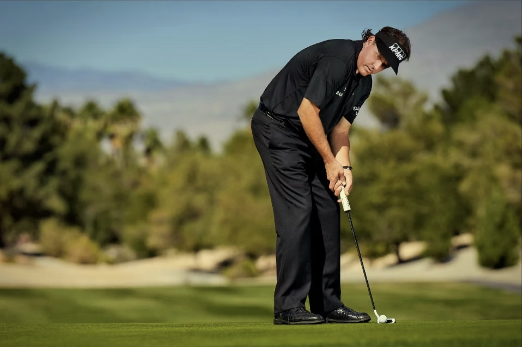 A man in golf attire preparing to putt on a golf course.