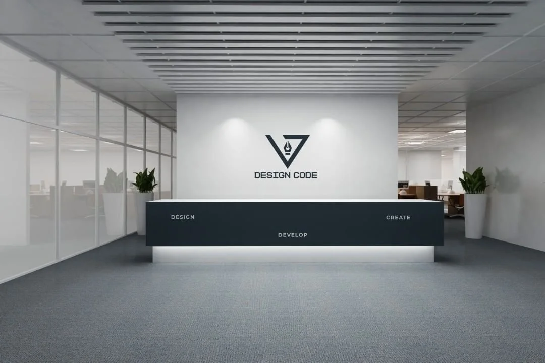 Modern office reception area with a white wall, black logo reading 'Design Code,' and a black counter with words 'Design,' 'Develop,' and 'Create,' flanked by tall white planters with green plants.