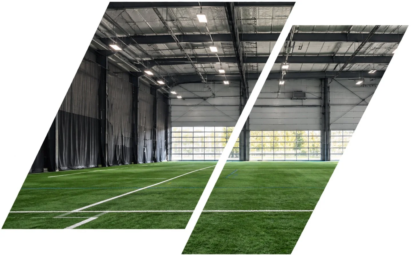 Indoor sports field with artificial turf, large windows, high ceiling, and overhead lighting, split into two sections.