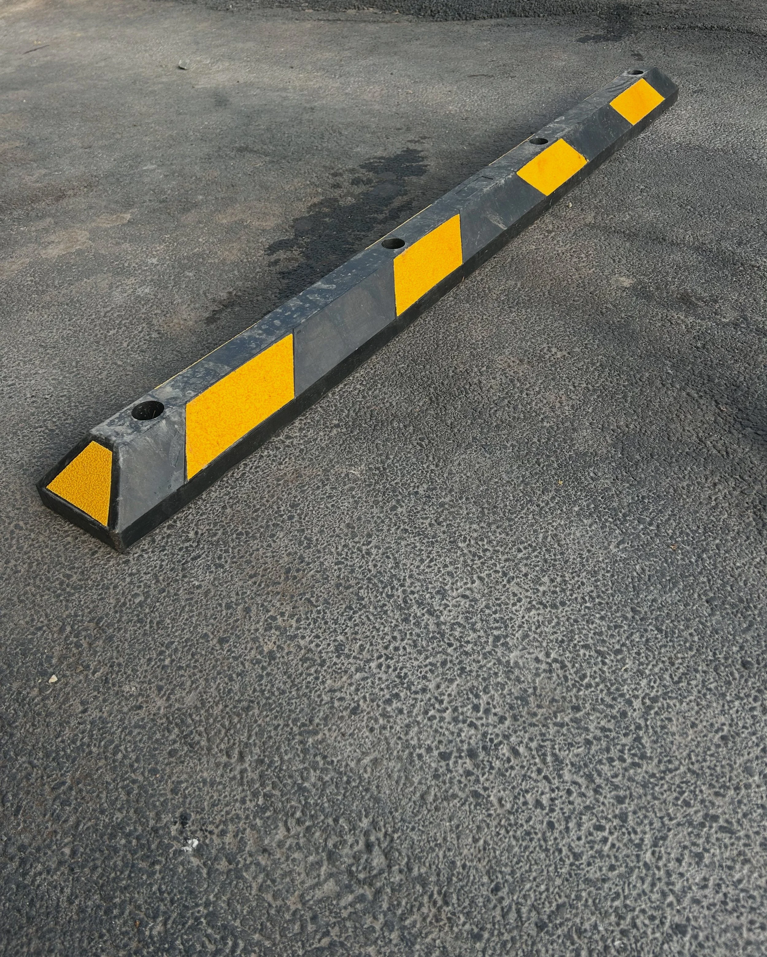 A black and yellow rubber parking bumper on asphalt ground.