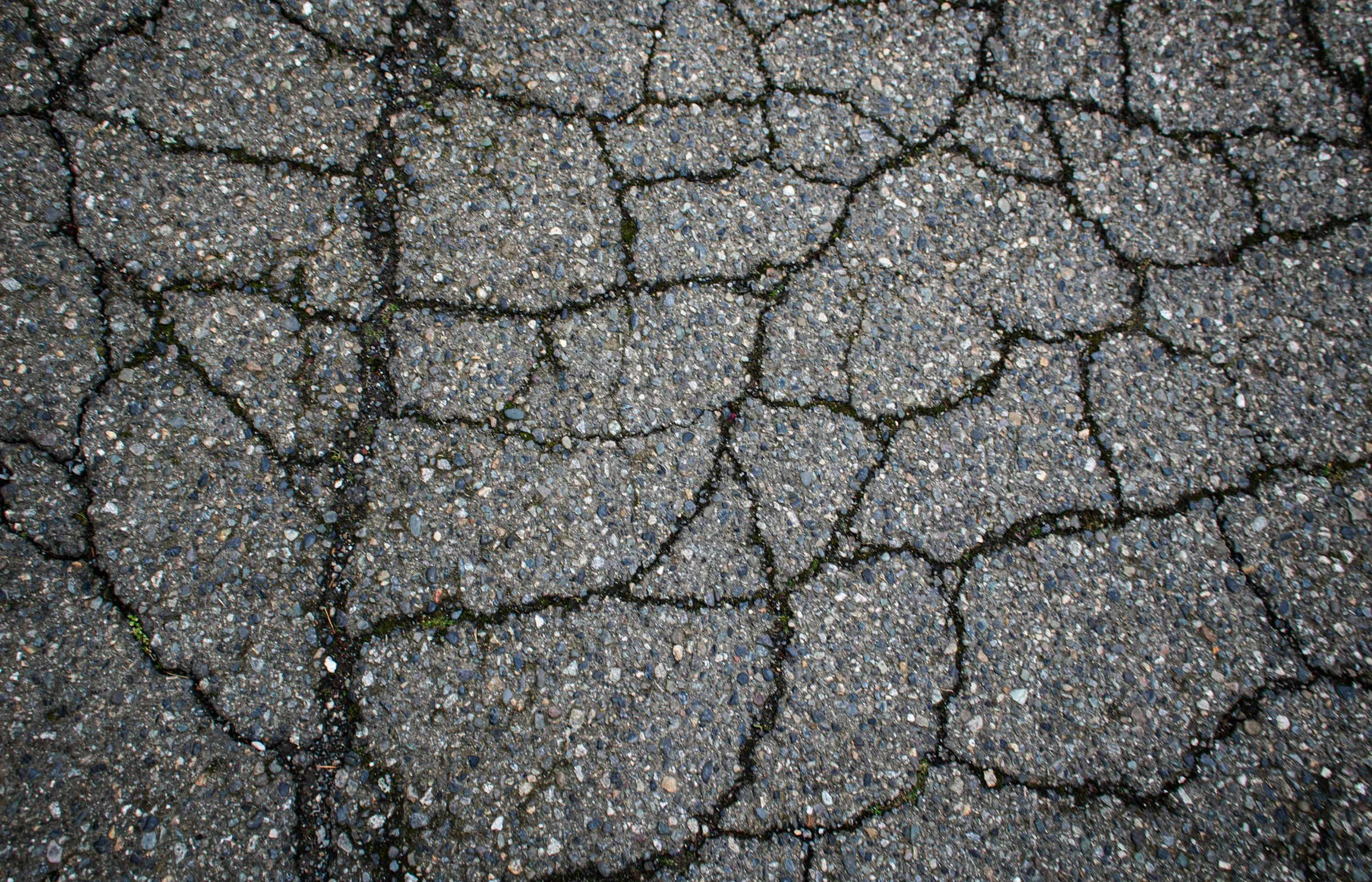 Close-up of cracked asphalt pavement surface with small gravel particles.