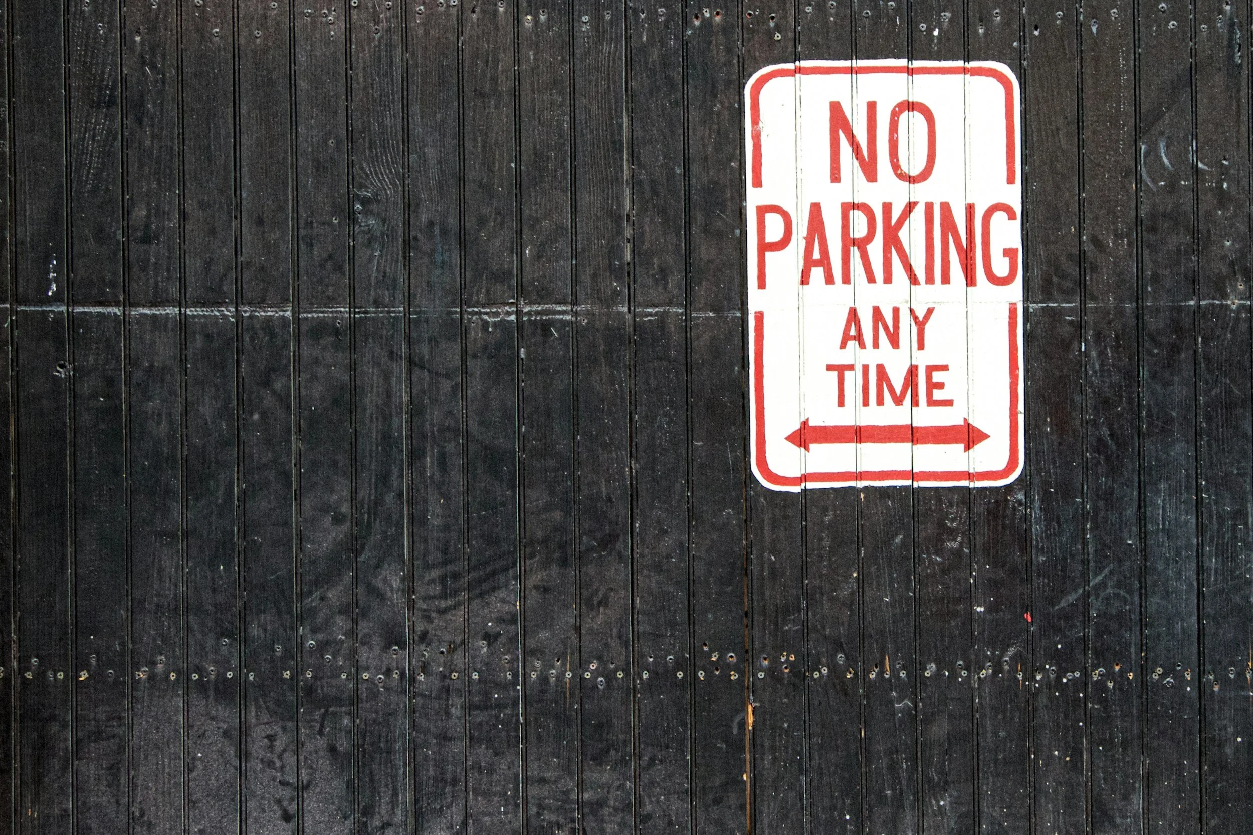 A red and white sign reading 'No Parking Any Time' mounted on a dark wooden wall.