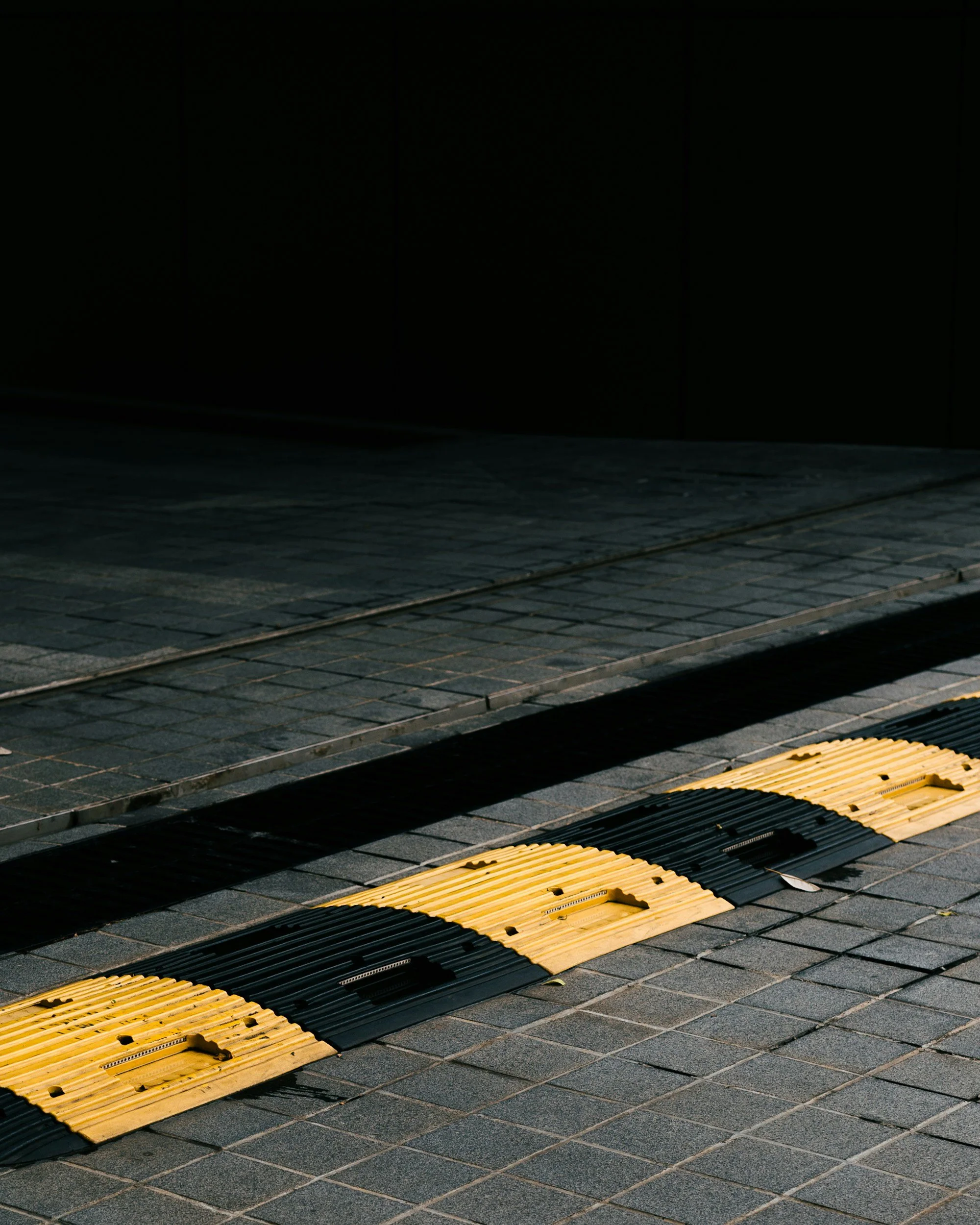 Close-up view of a yellow and black tactile paving strip installed on a brick sidewalk, used for visually impaired pedestrians.