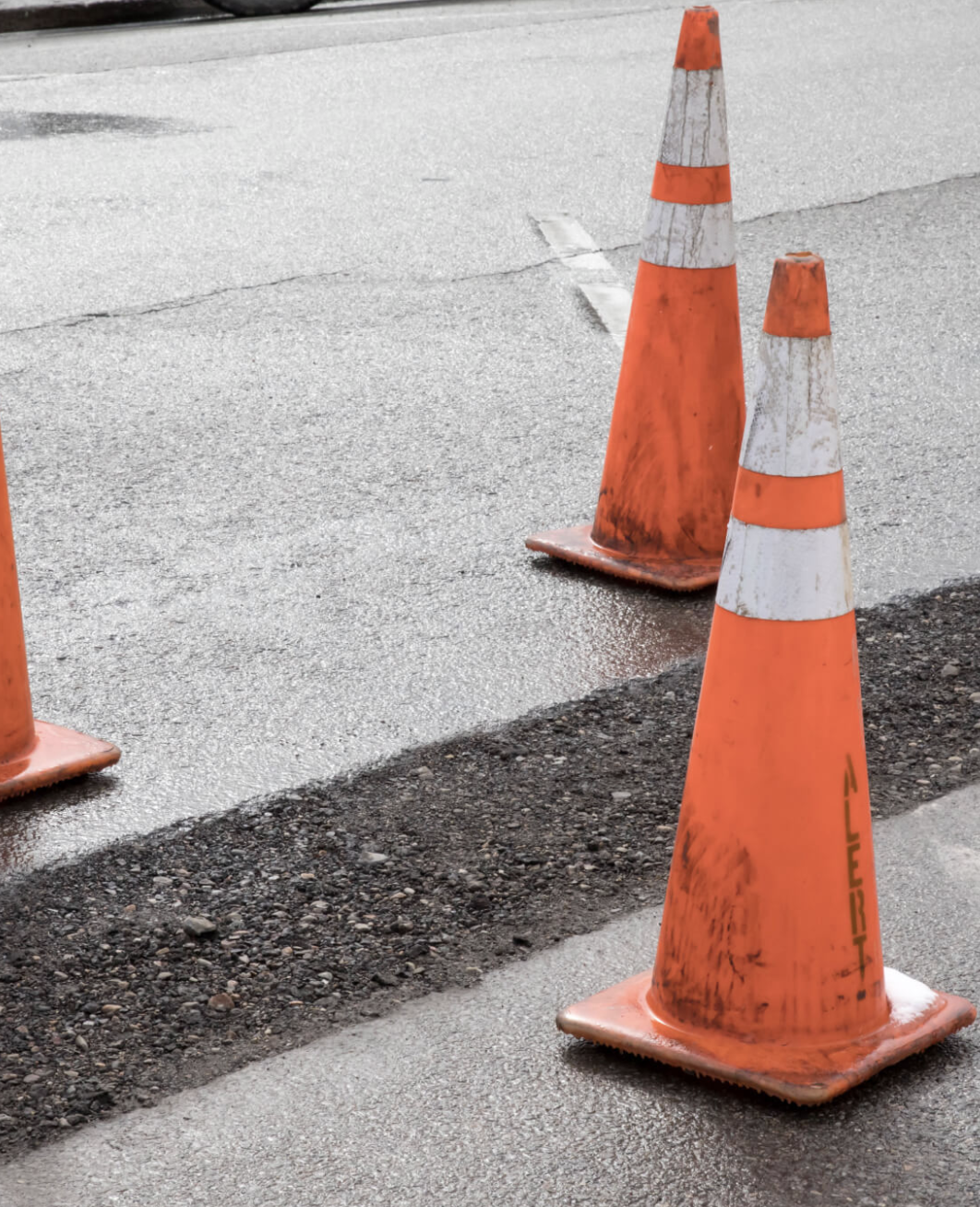 Two orange traffic cones on a wet road, marking a construction or repair area.