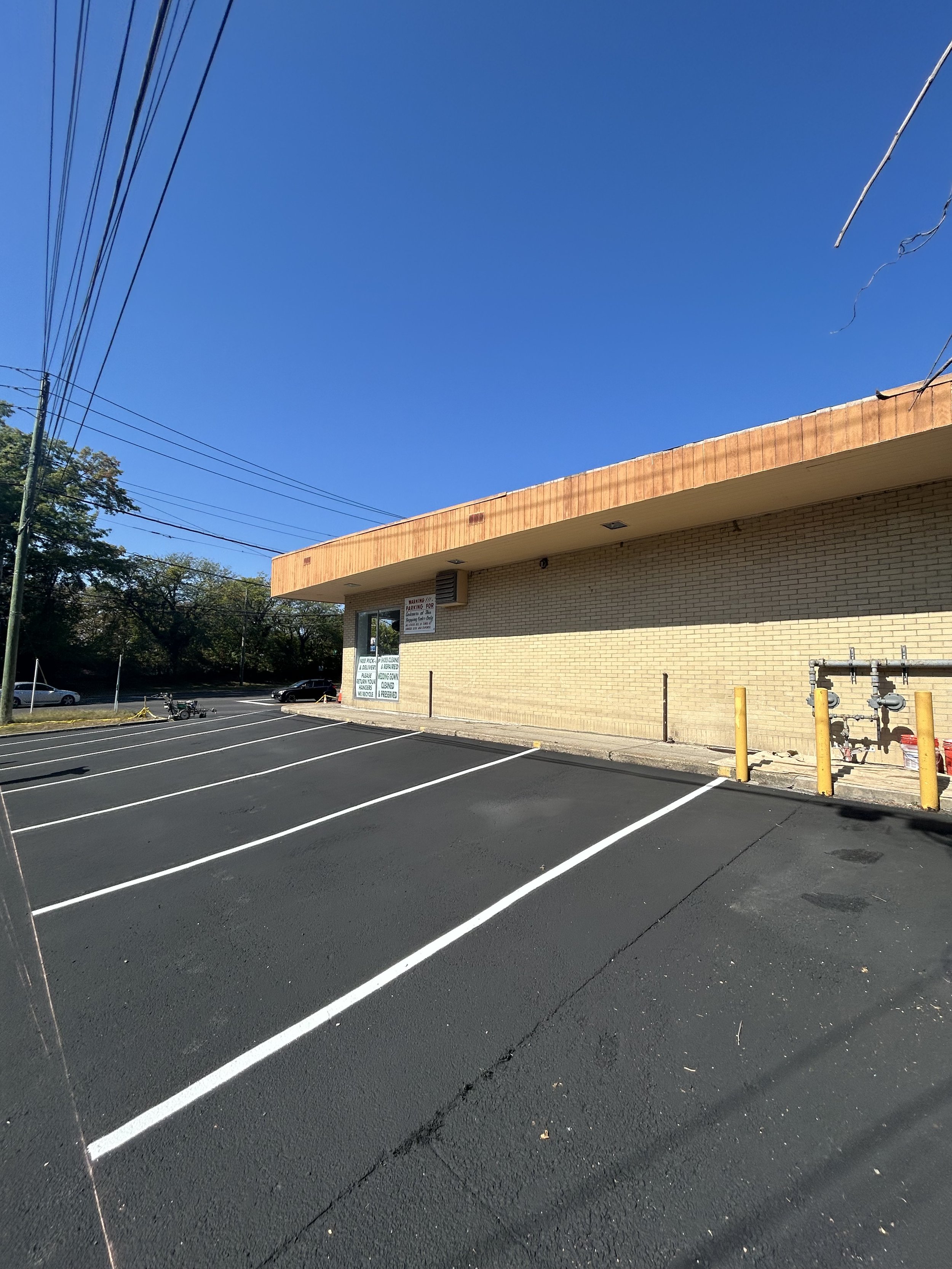Empty parking lot with freshly painted white lines and a brick building in the background under a clear blue sky.