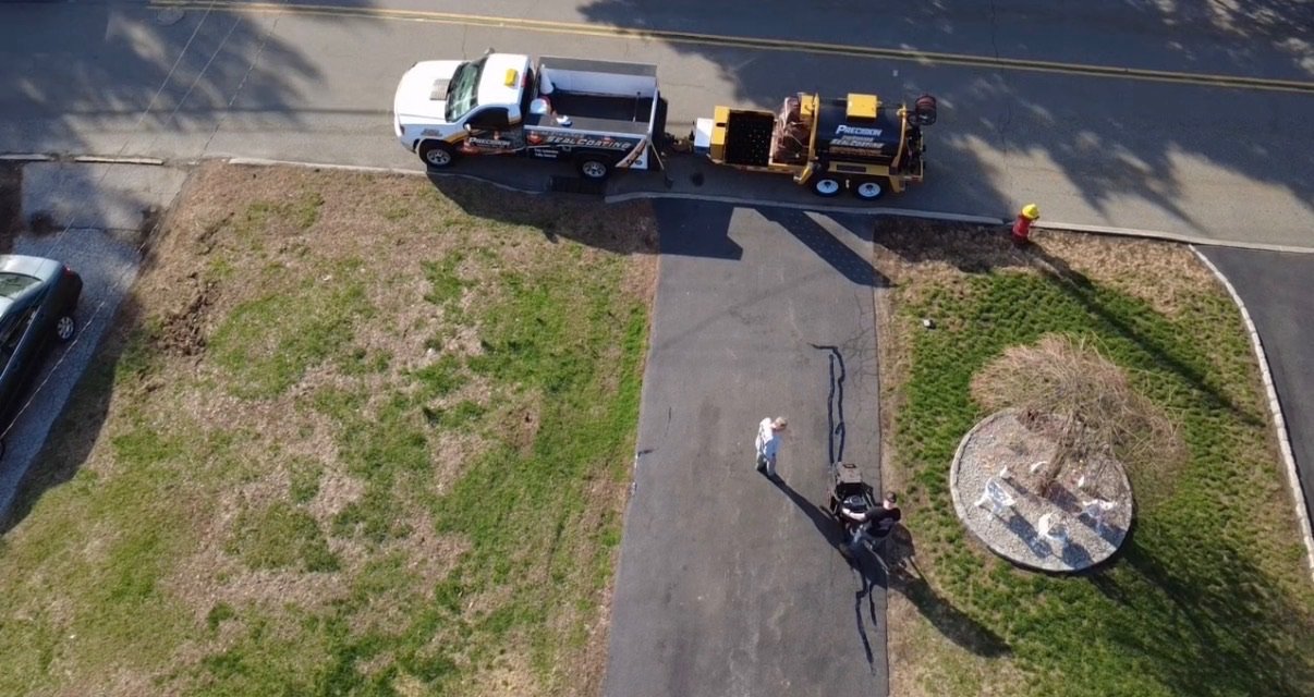 Aerial view of a lawn and walkway with a pickup truck, trailer, and workers on a sunny day.