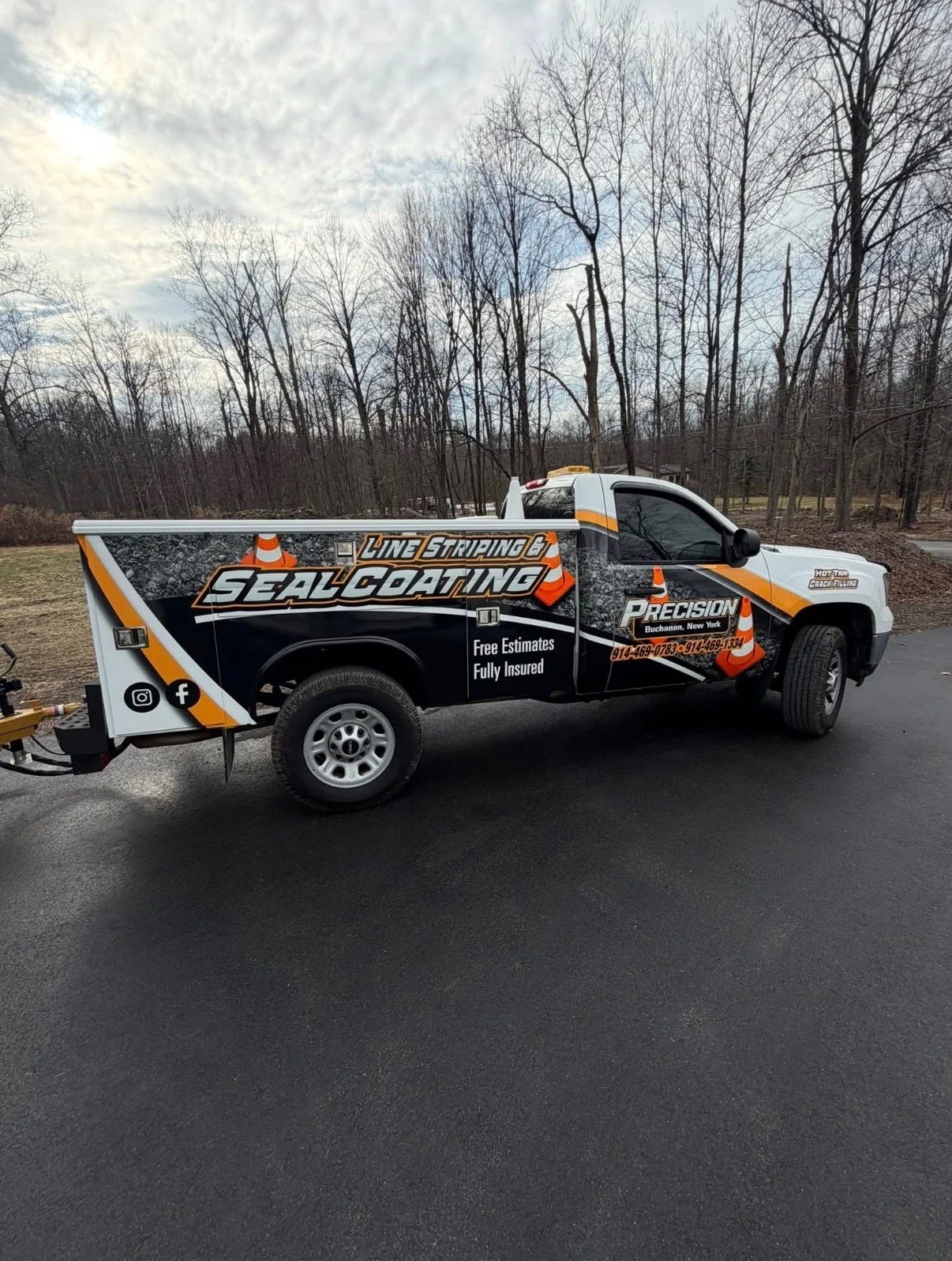 A service truck with graphic decals advertising line striping and seal coating, parked on a paved surface with leafless trees in the background.