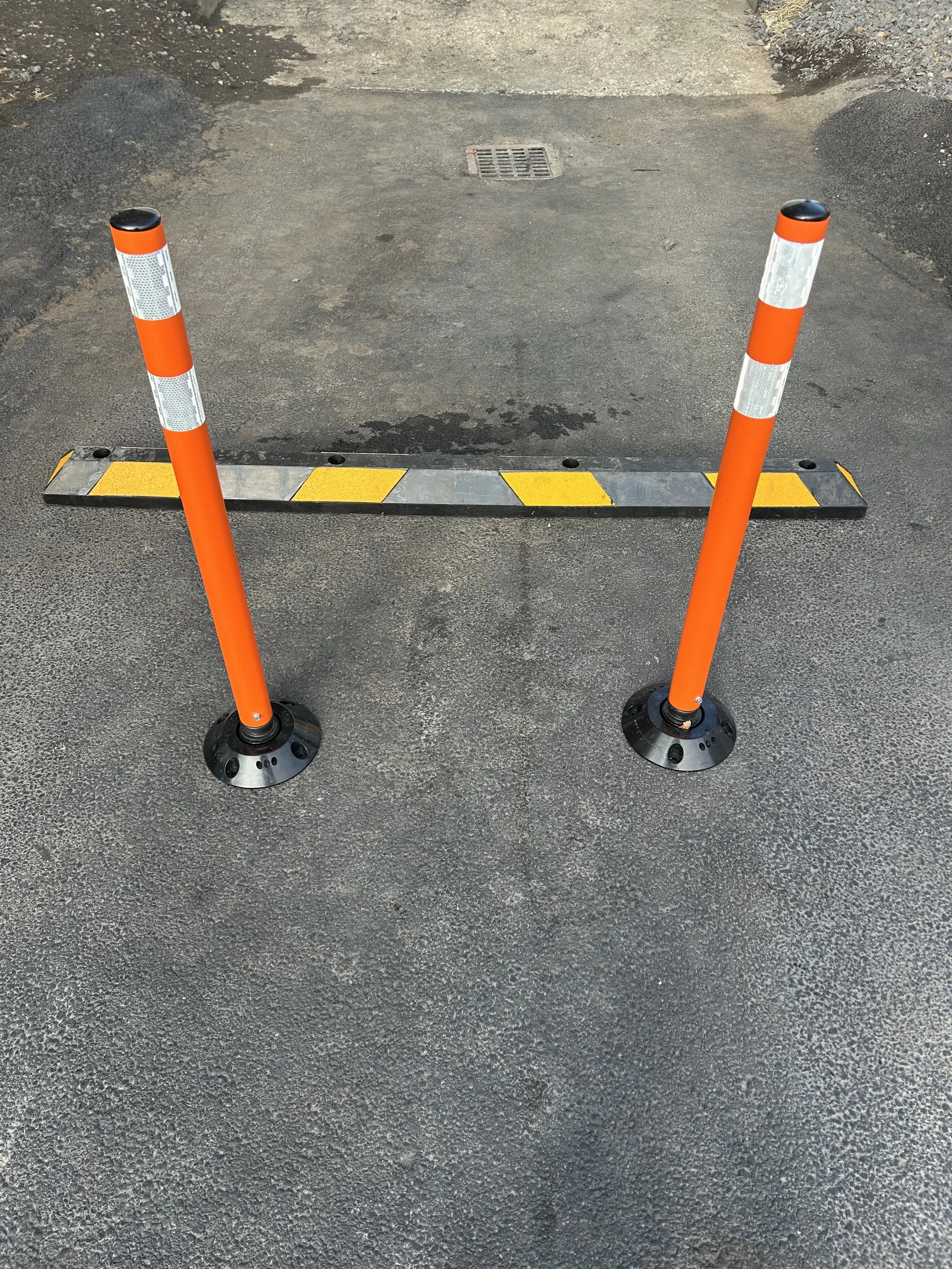 Two orange and white traffic cones blocking access to a parking space with yellow and black striped barrier on asphalt ground.