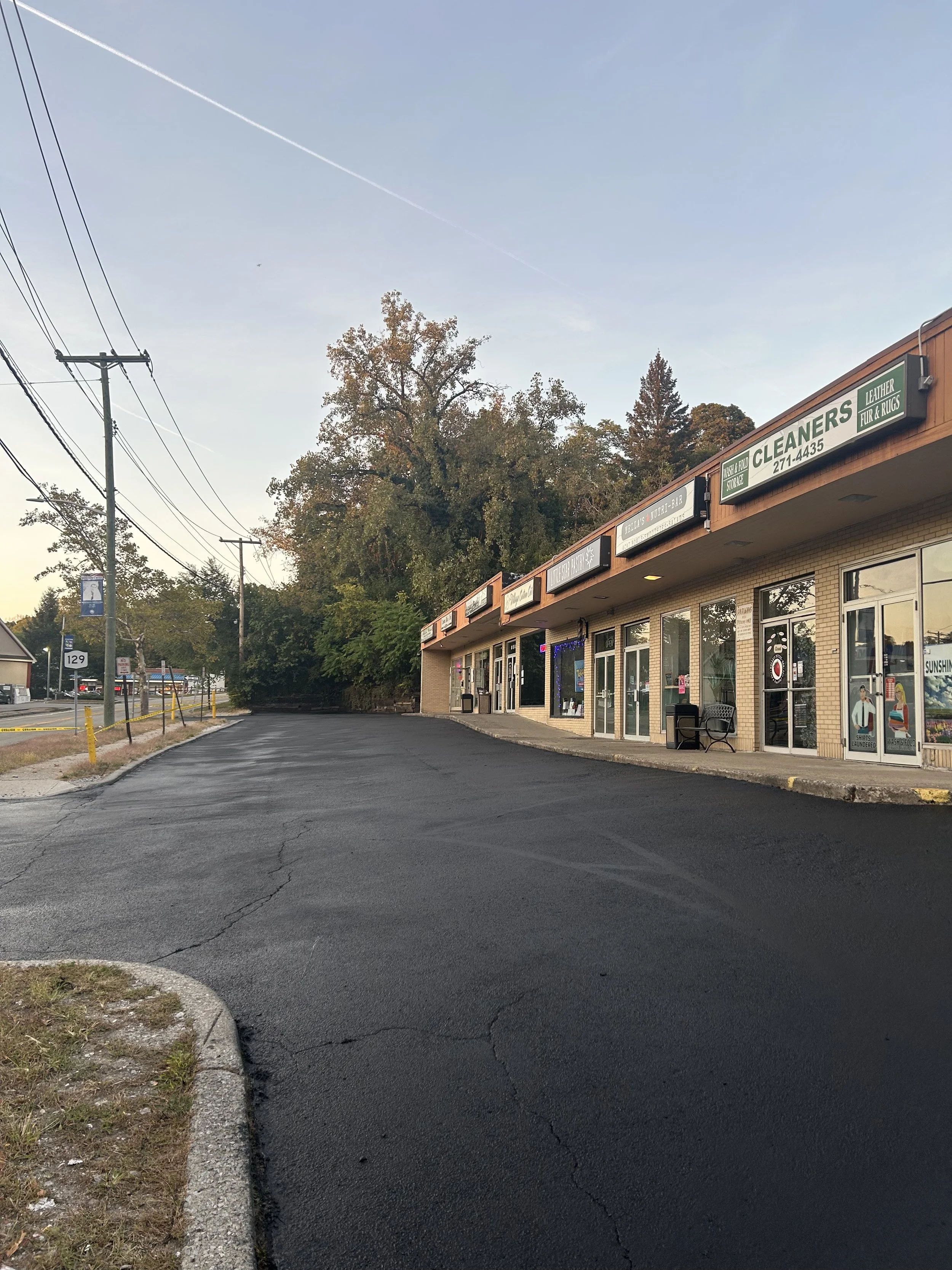Empty parking lot in front of strip mall with multiple storefronts, including a cleaning business, under a clear sky.