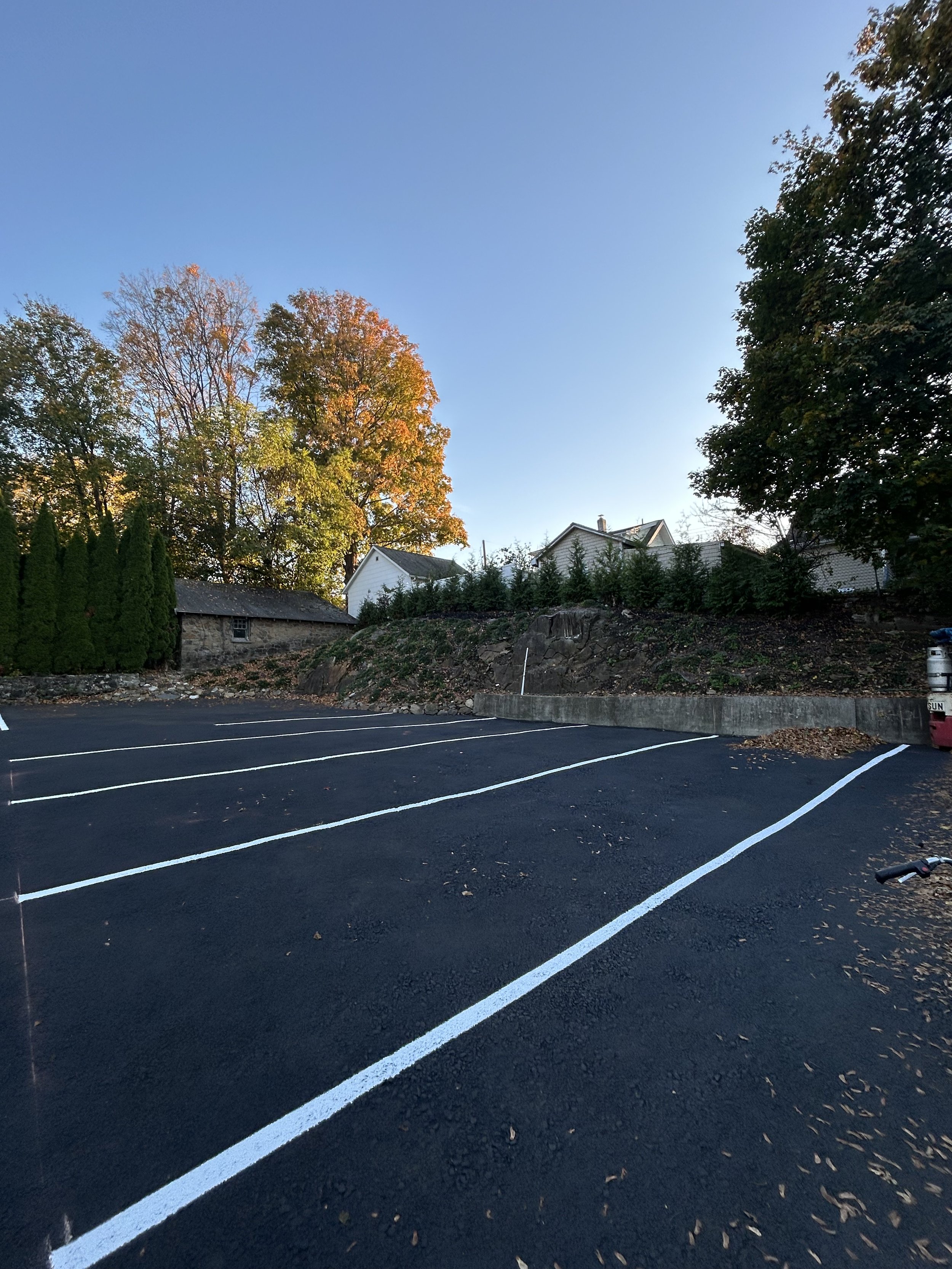 Empty parking lot with freshly painted white lines, surrounding trees with fall foliage, residential houses in the background, and a bike handlebar visible on the right side.