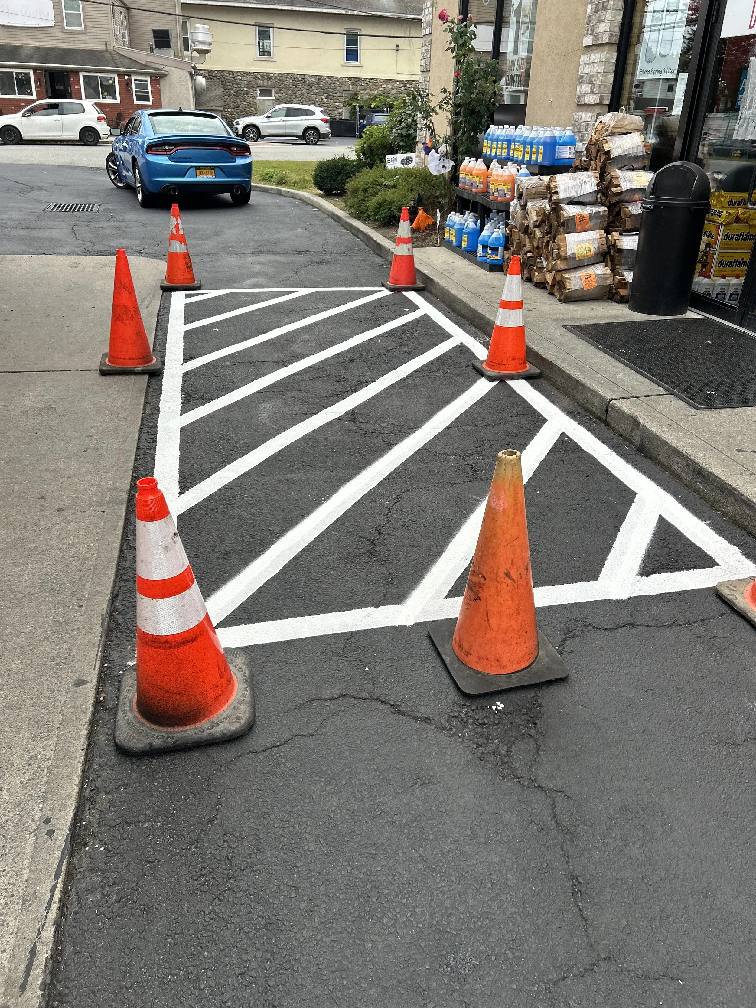 A parking space temporarily closed with orange cones and white painted lines, near a store entrance with supplies and a trash bin.