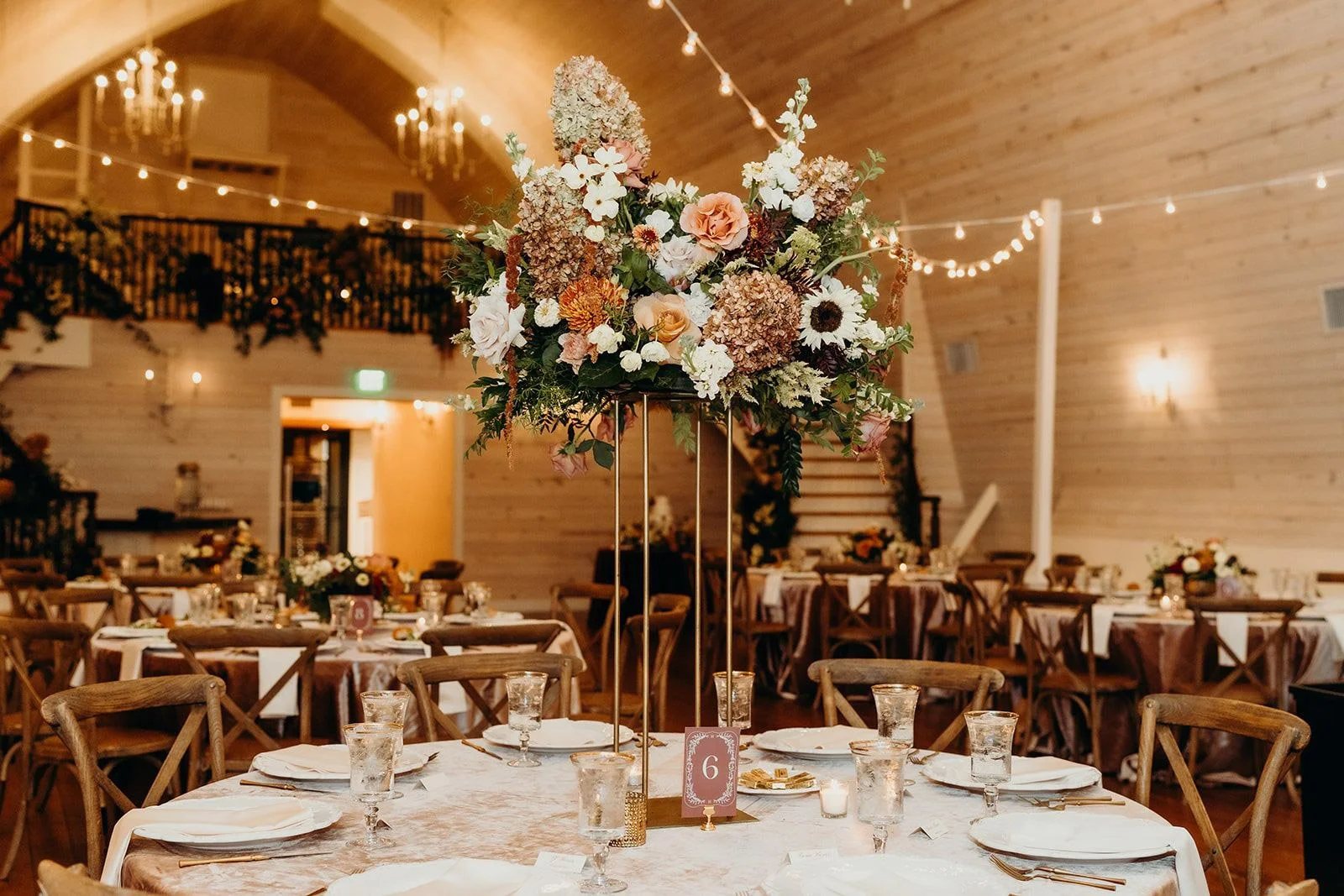 Tall reception centerpiece of limelight hydrangea, roses, sunflowers, and dahlias over velvet linens inside The Wakefield Barn near Raleigh