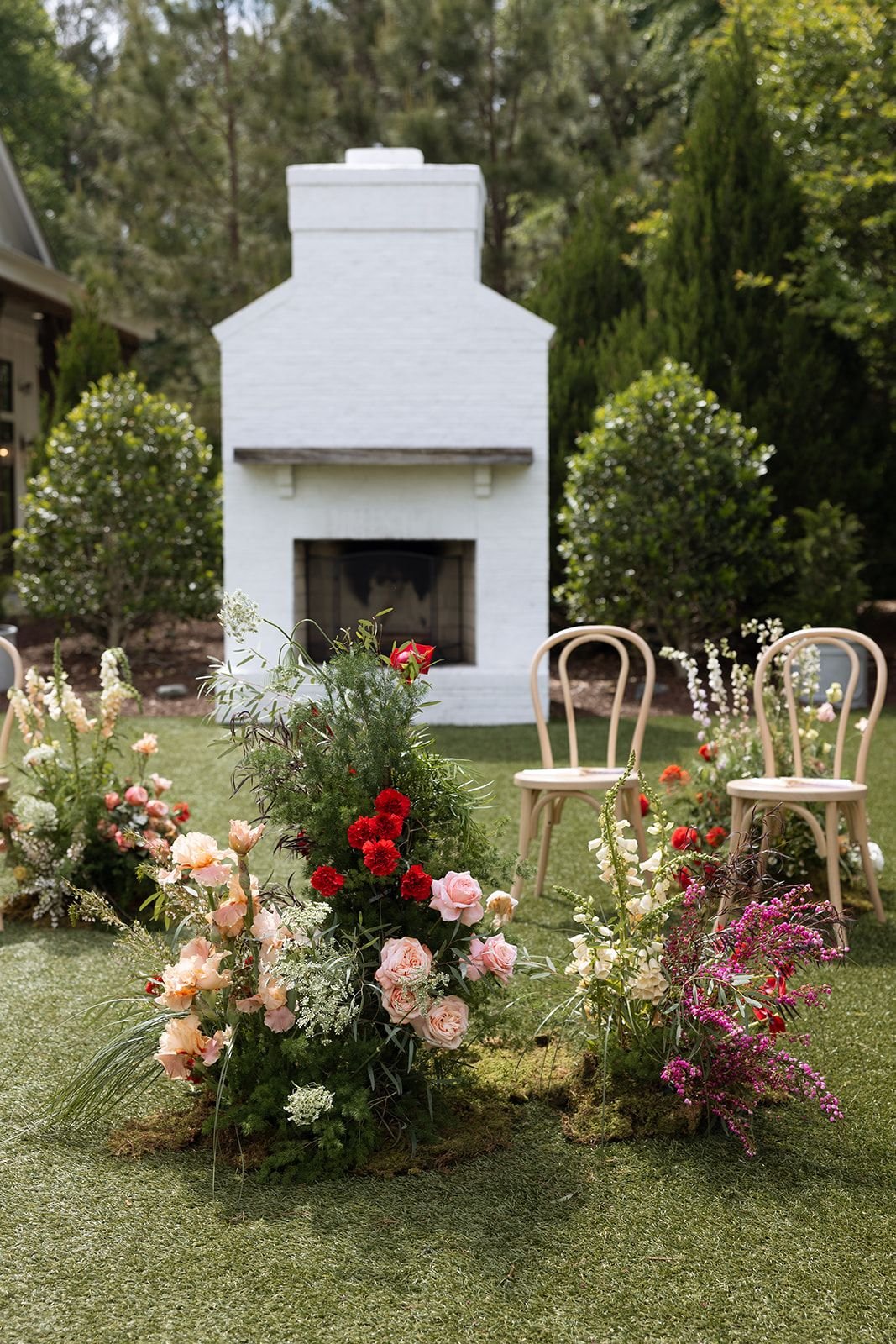 Outdoor wedding setup with chairs, floral arrangements, and a white brick outdoor fireplace in the background.