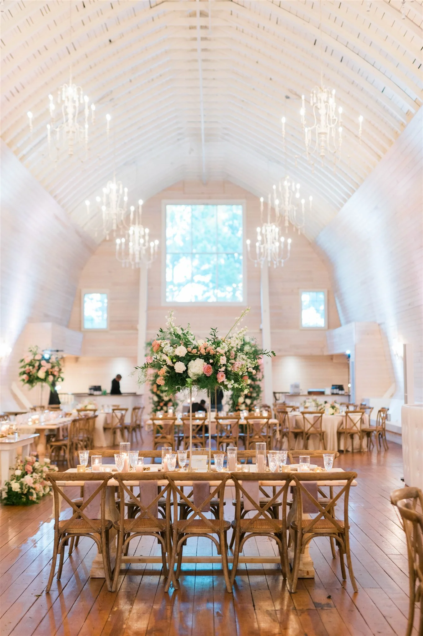 Elegant wedding reception inside a wooden chapel with high arched ceiling, chandeliers, large window, and floral centerpieces on the tables.
