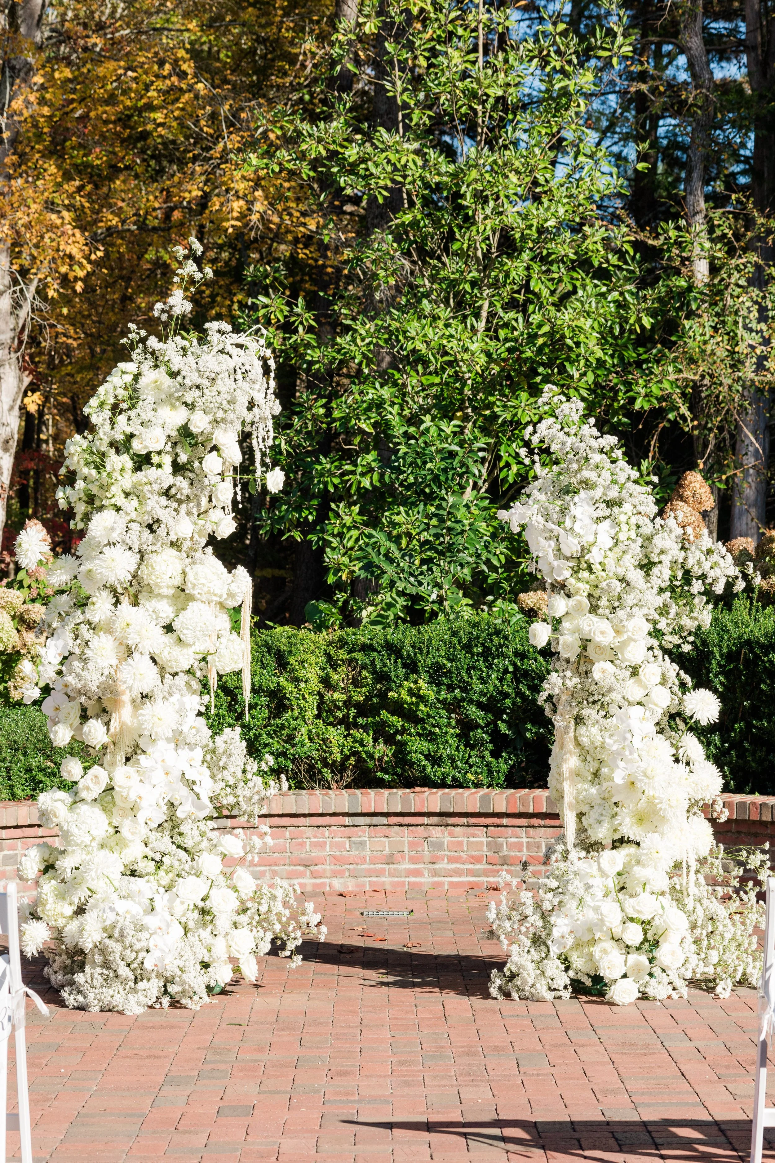 Asymmetrical white floral ceremony installation set in the gardens at The Barn of Chapel Hill