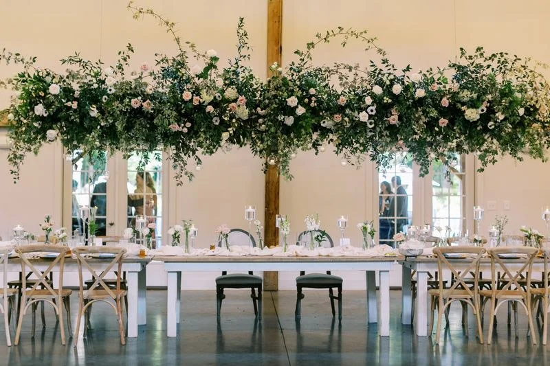 Wedding reception head table with a lush hanging floral installation inside The Barn of Chapel Hill