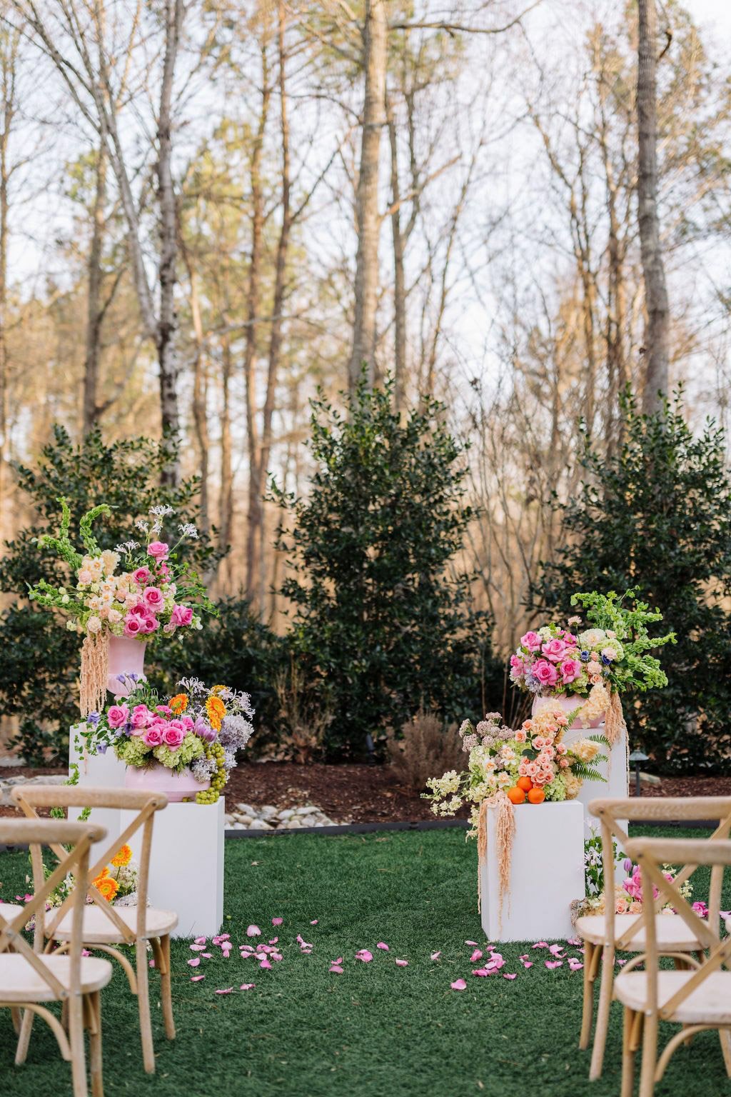 Colorful garden-inspired ceremony florals designed by Wild Flora Flowers at Carolina Grove, featuring lush floral pedestals with roses, ranunculus, seasonal blooms, and organic greenery framing an outdoor wedding ceremony.