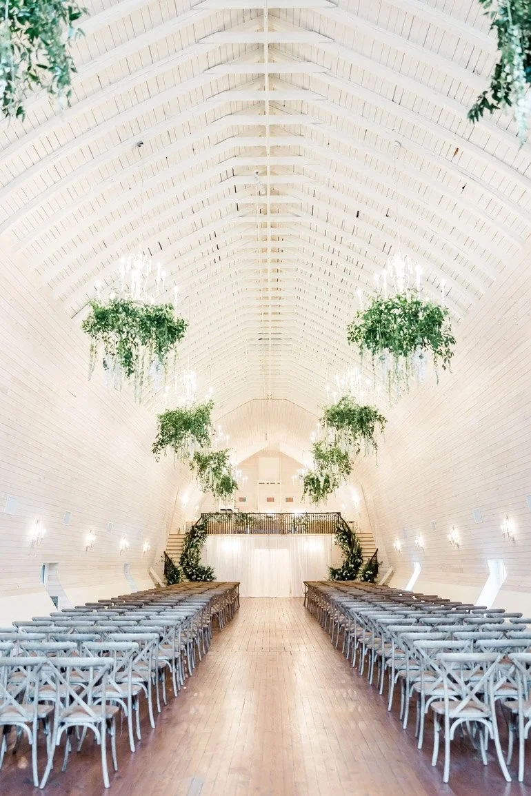 Wedding ceremony inside Historic Wakefield Barn featuring lush hanging greenery installations and aisle florals suspended from chandeliers, showcasing elevated floral design by a North Carolina wedding florist.