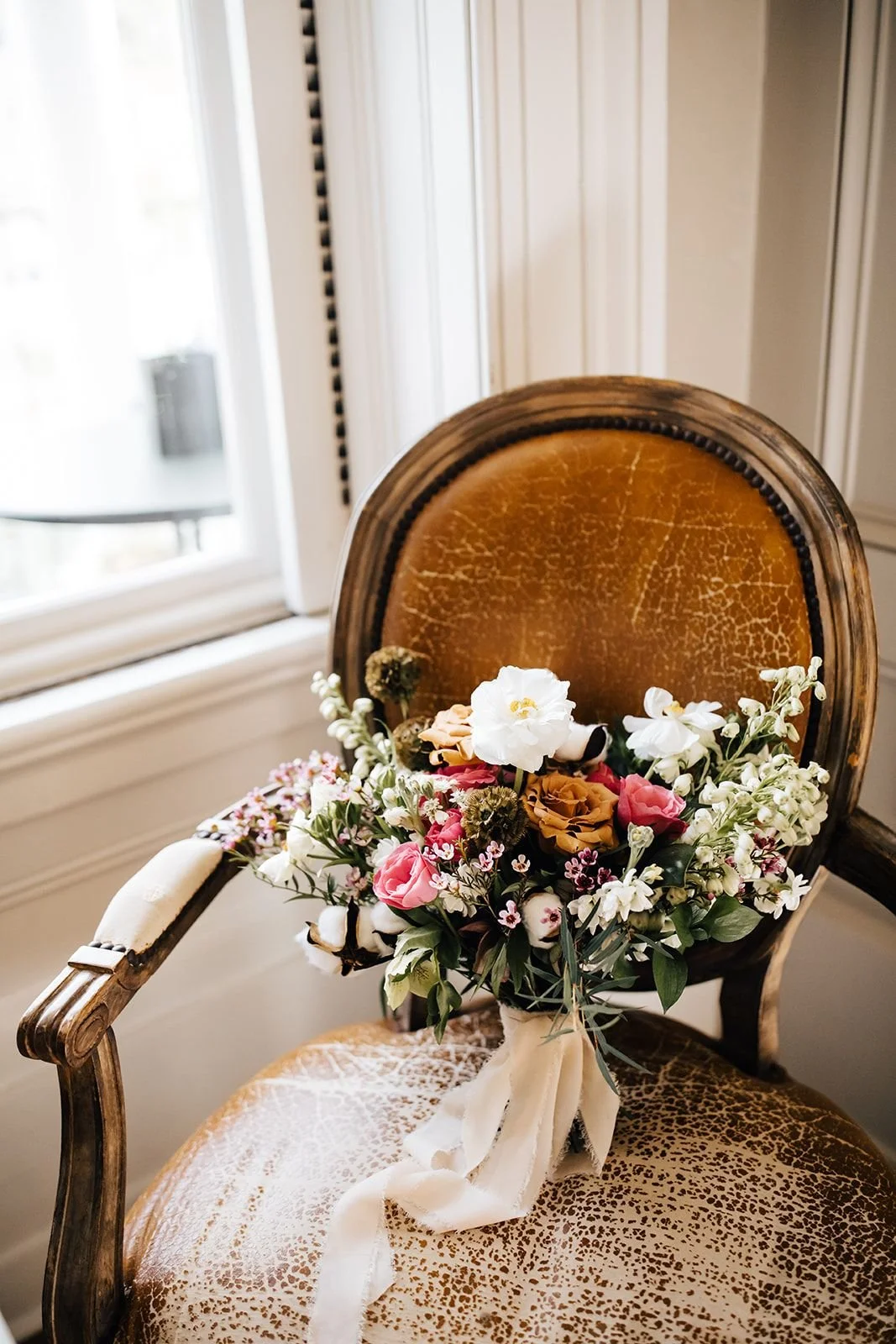 Garden-style bridal bouquet with blush and white flowers resting on a vintage upholstered chair in a light-filled Raleigh wedding venue
