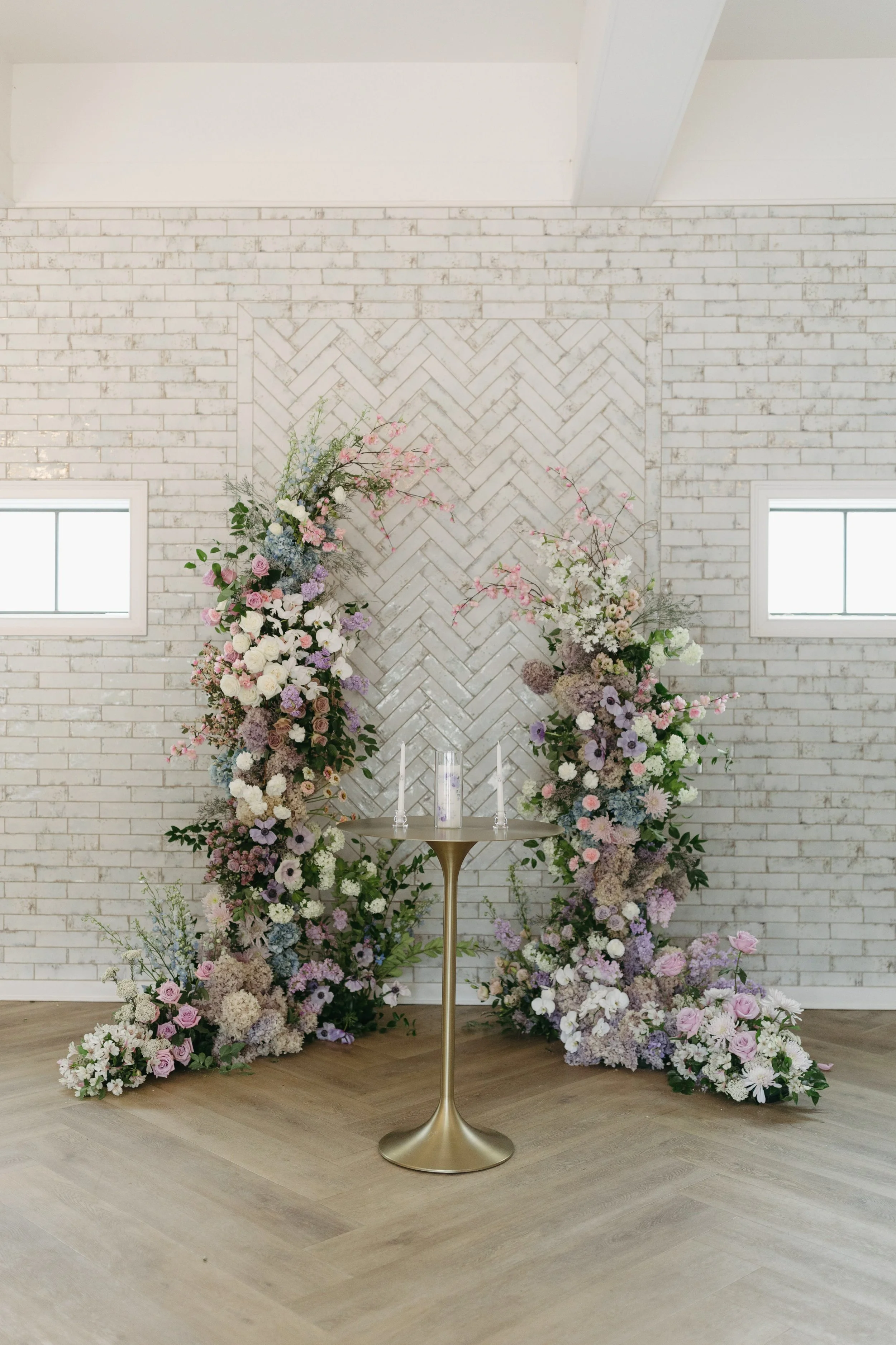 Indoor wedding ceremony installation at The Bradford featuring a lush, asymmetrical floral arch in soft pastel tones and seasonal blooms, designed by Wild Flora Flowers to frame an intimate ceremony setting