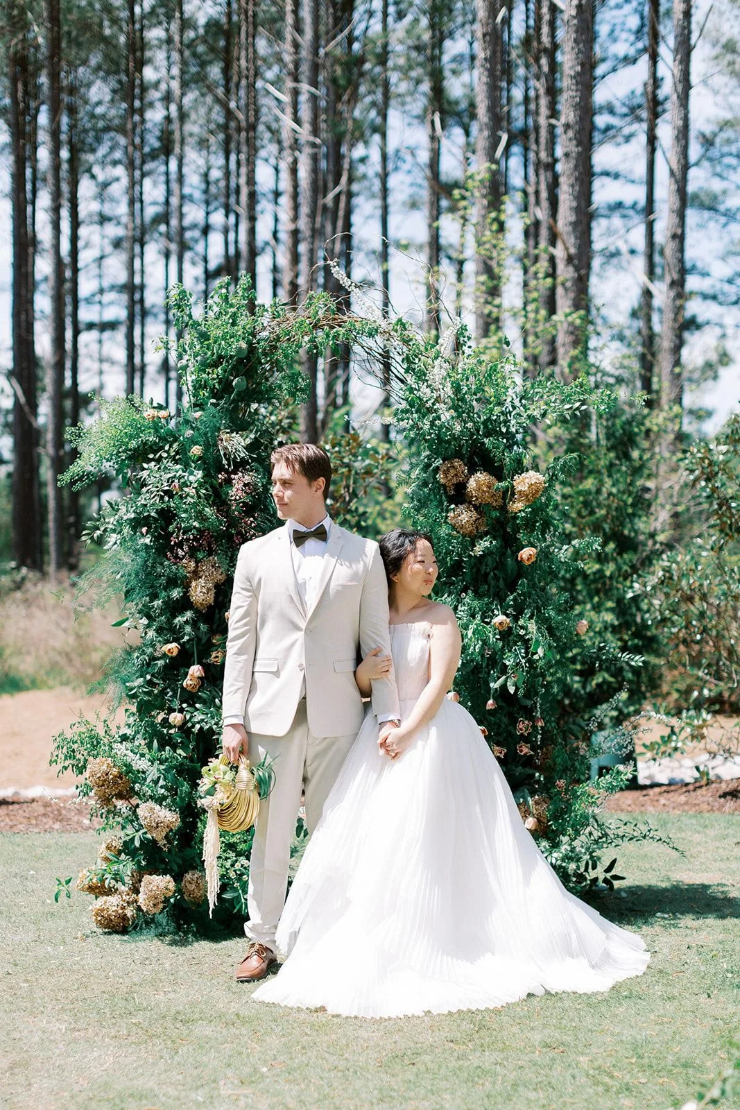 Bride and groom standing beneath a lush, garden-style floral arch designed by Wild Flora Flowers at The Upchurch wedding venue in Raleigh, North Carolina.
