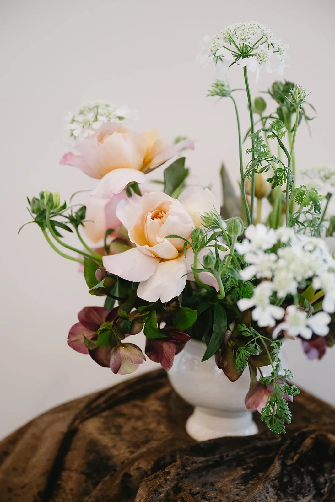 A floral arrangement with light pink and white flowers in a white vase on a wooden surface.