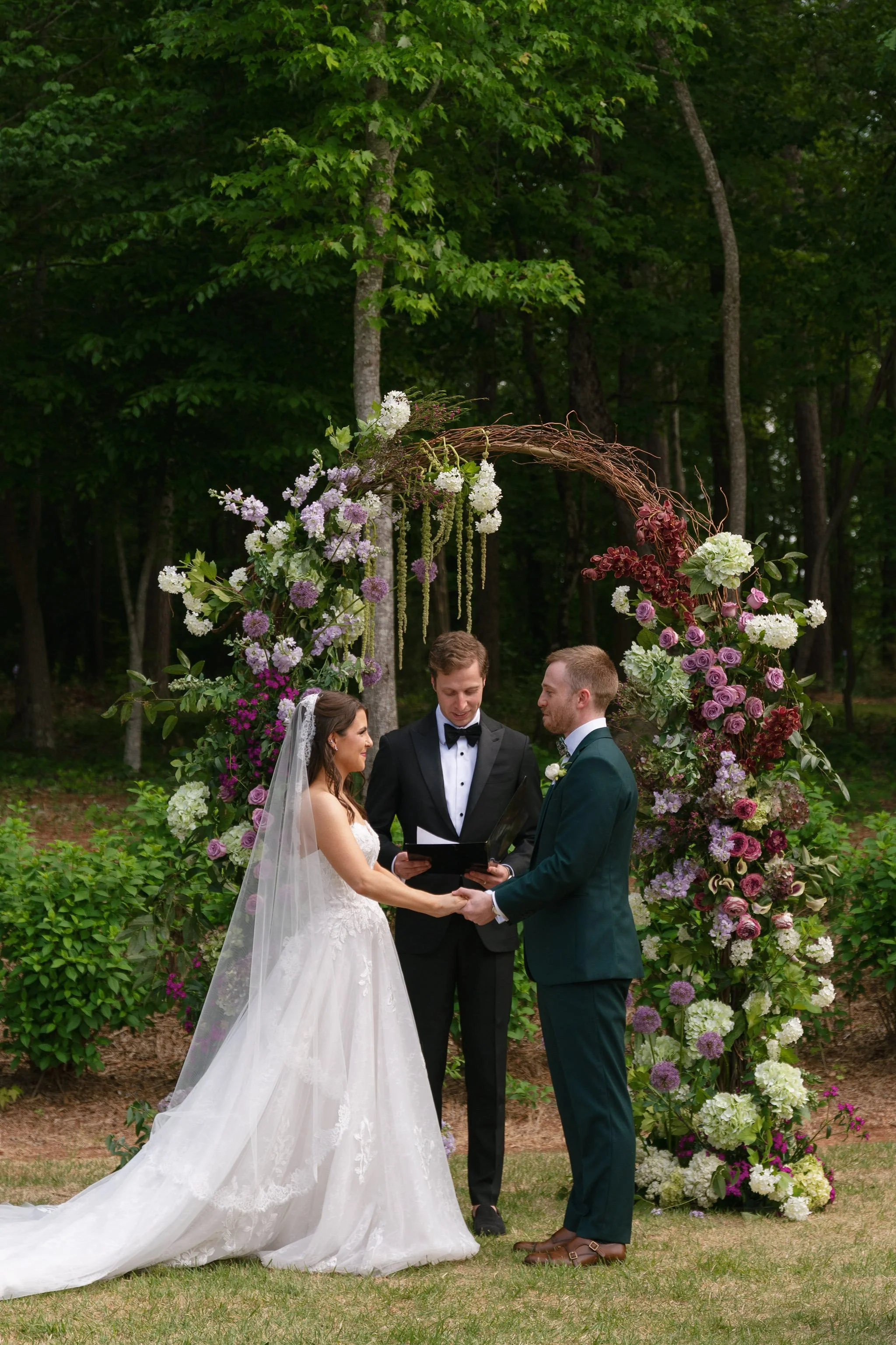  Bride and groom holding hands at their floral arch during the ceremony at The Barn of Chapel Hill 