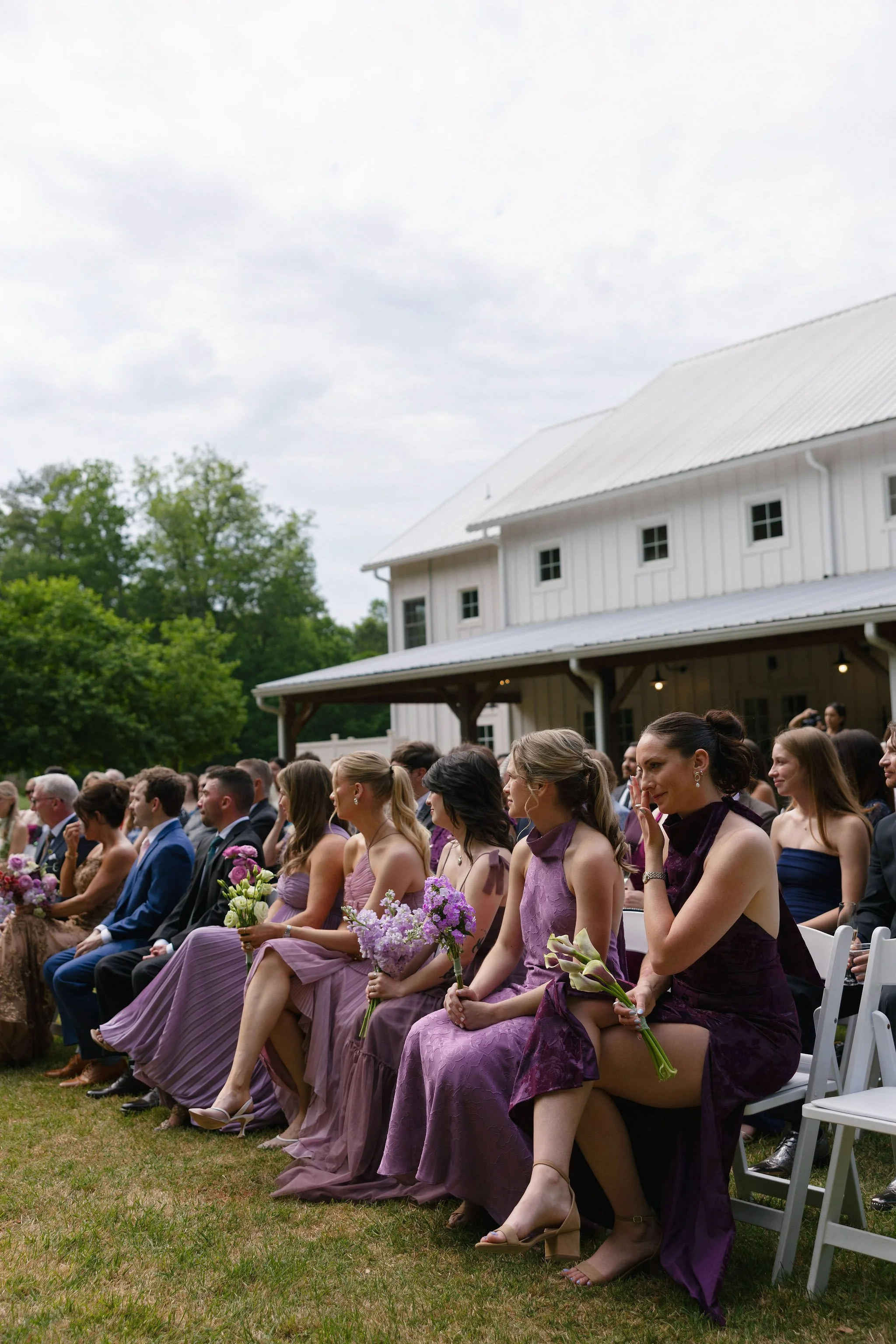  Bridesmaids in purple holding lavender and calla lily bouquets in front of the white barn 