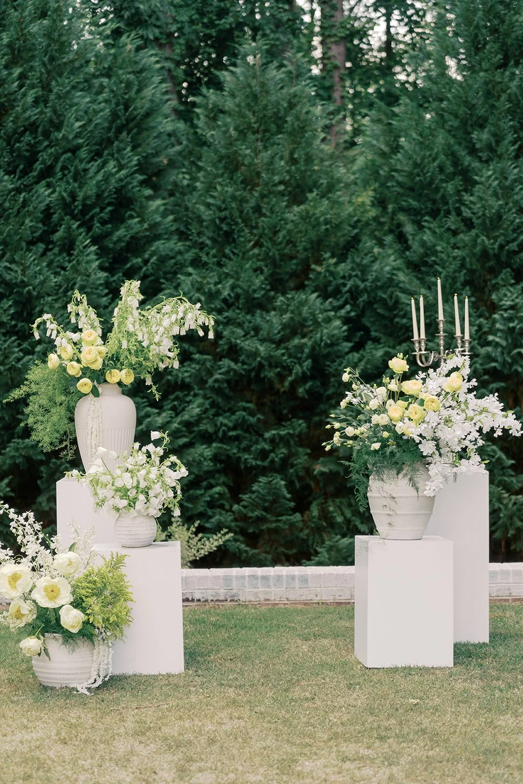  Modern luxury ceremony arrangements of white garden roses, campanula, and greenery in urns on white pedestals with a silver candelabra at The Bradford 