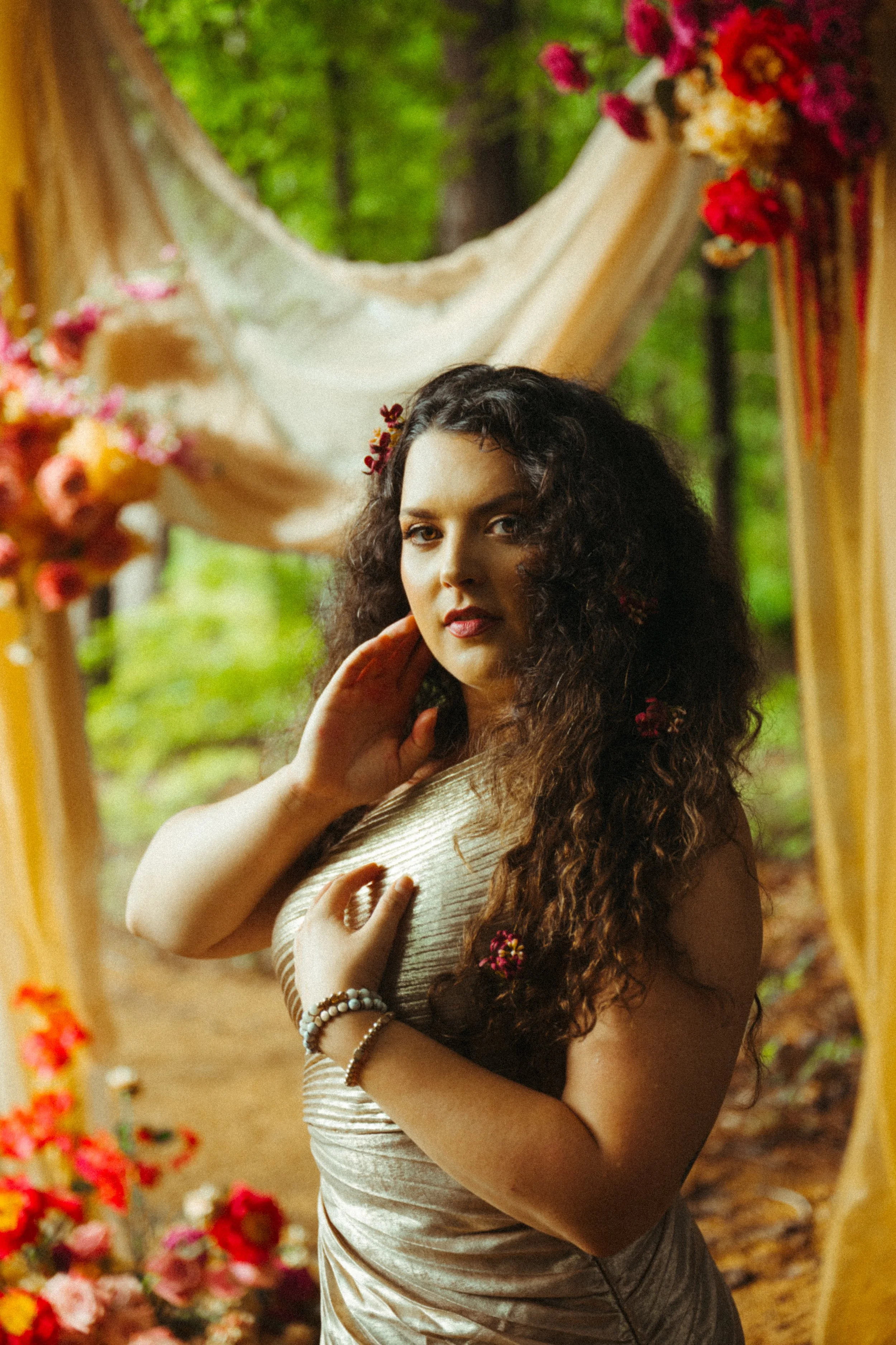 A woman in traditional attire looking at herself in a mirror, surrounded by flowers and greenery.